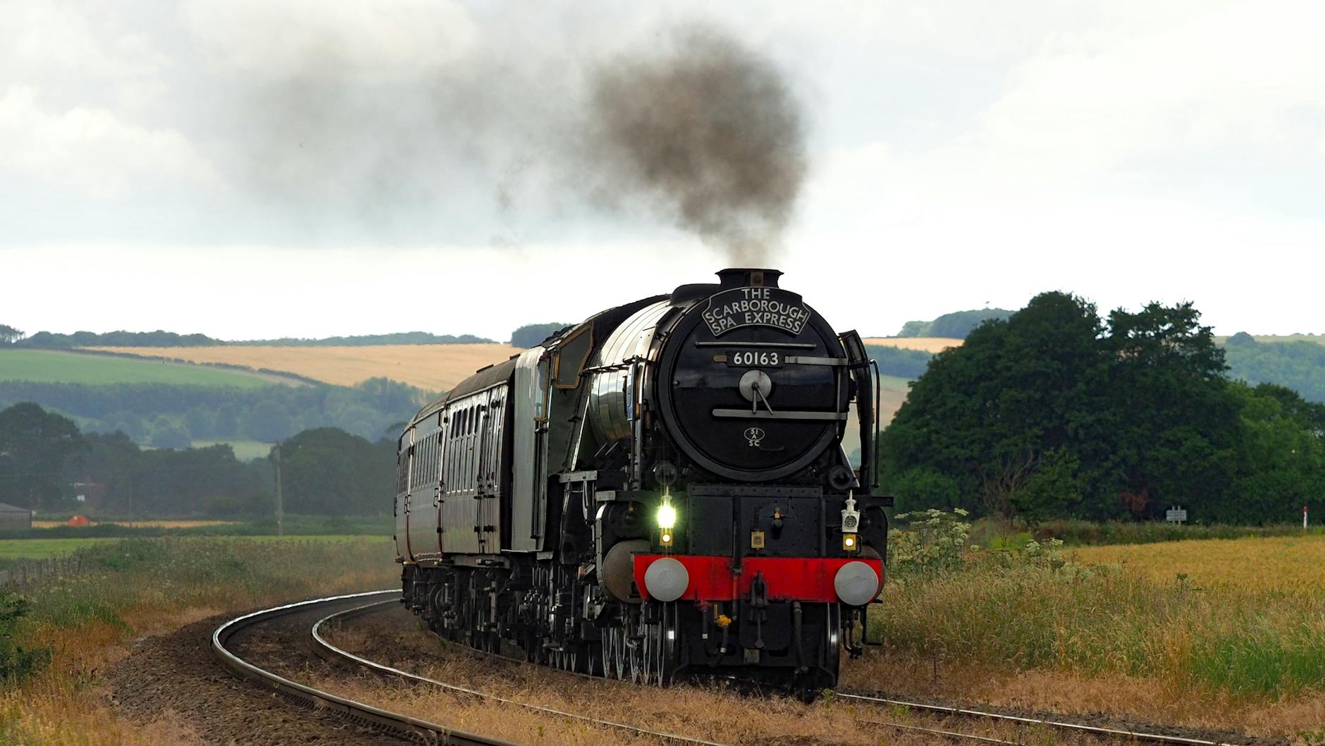 A steam locomotive pulling carriages through green countryside on a heritage railway