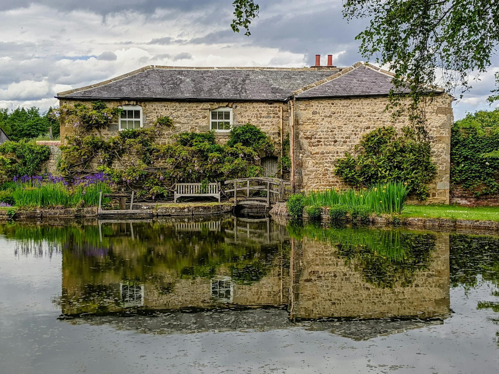 A honey-stone holiday cottage in the Cotswolds countryside surrounded by gardens