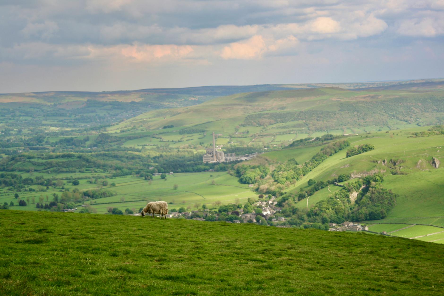 A panoramic view across a green Cotswolds valley from the escarpment ridge