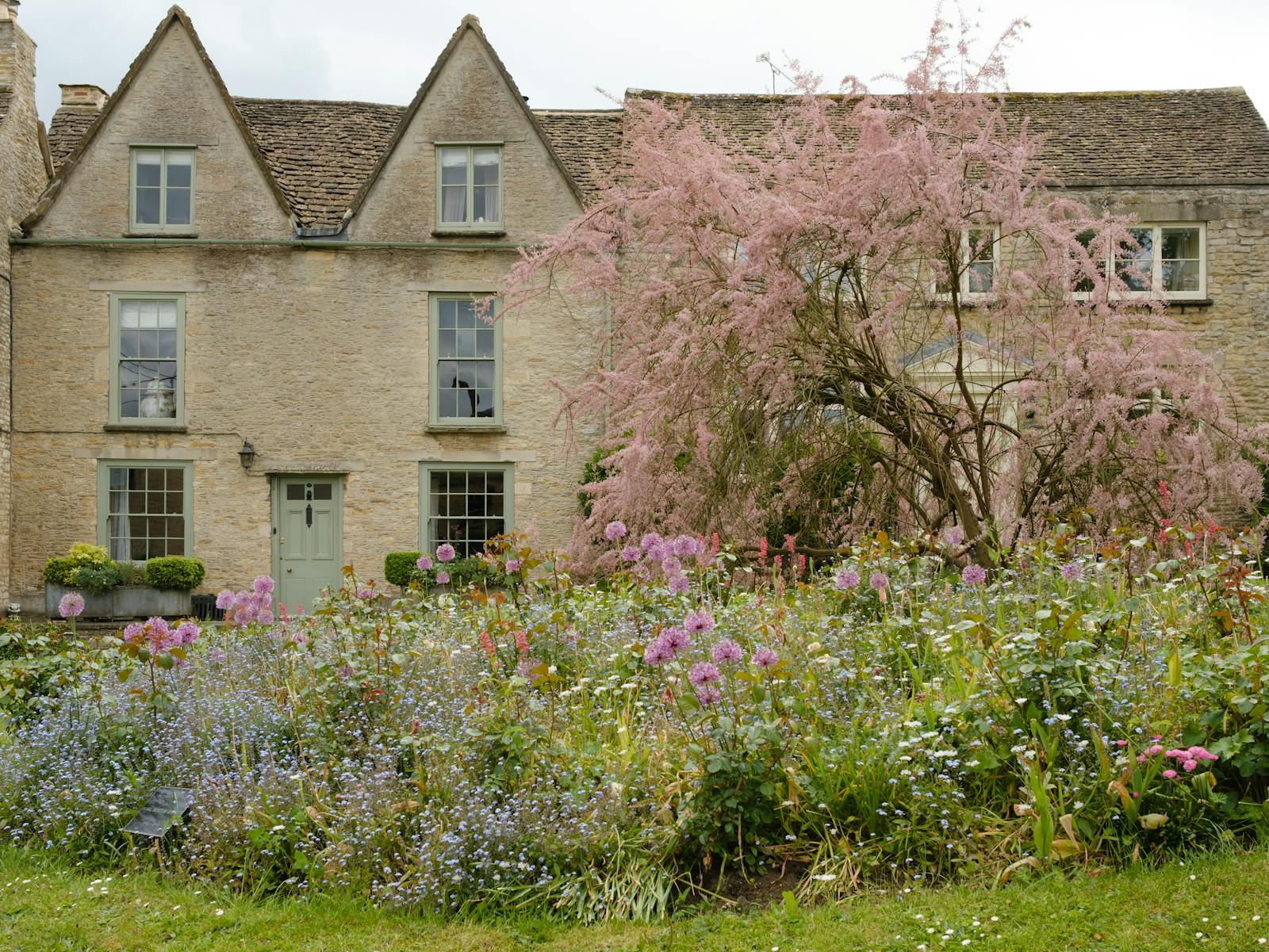 A honey-stone cottage framed by a lush spring garden of pink and purple flowers
