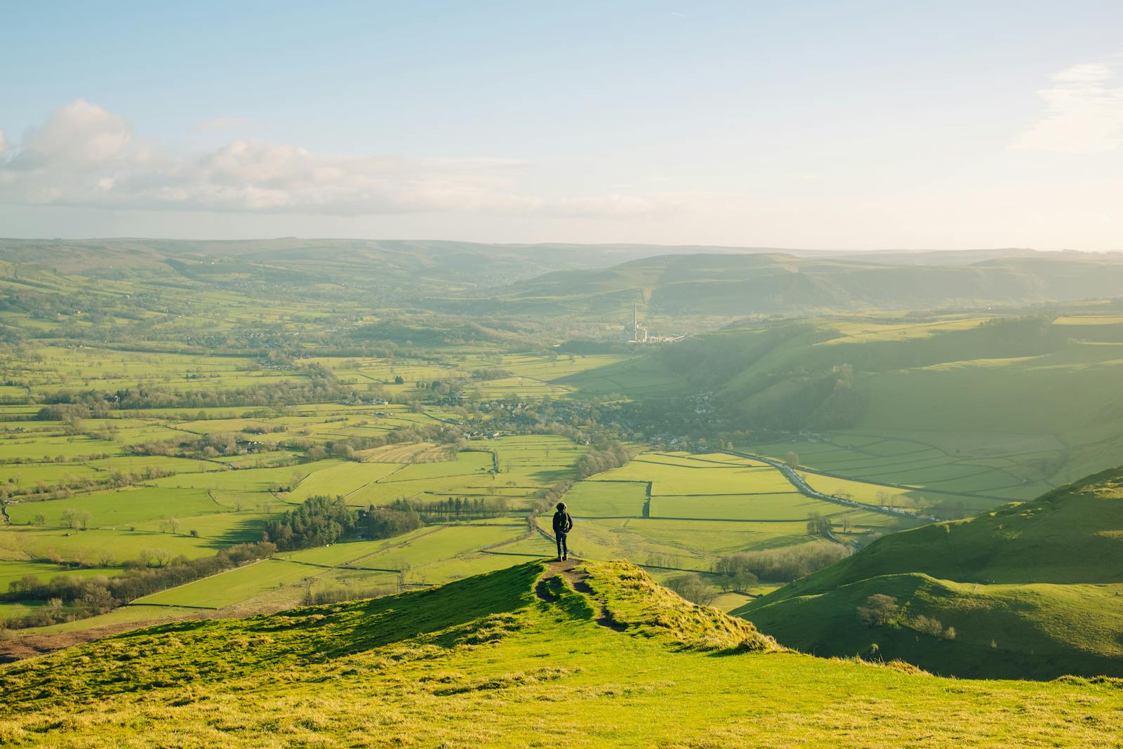 A lone walker standing on a hilltop gazing over vast green English countryside