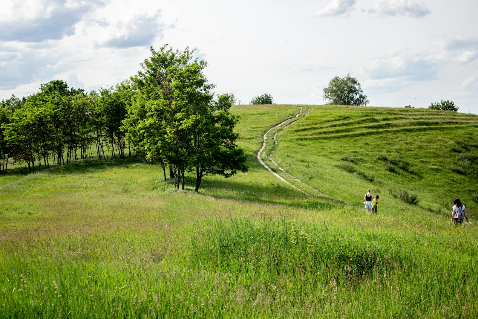 People walking on lush green hills under a cloudy sky