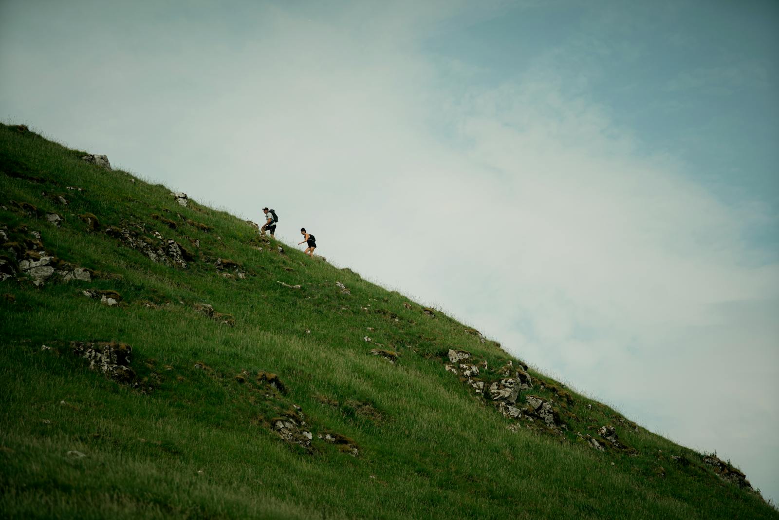 Two hikers ascending a grassy green hill under a blue sky in England
