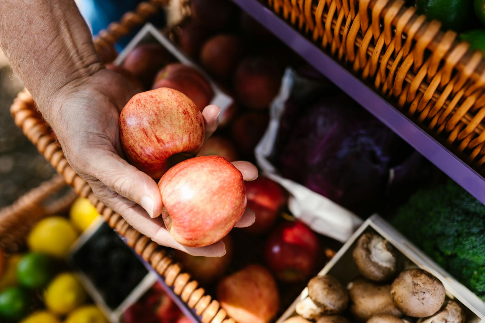A hand holding fresh apples at a colourful farm shop produce display