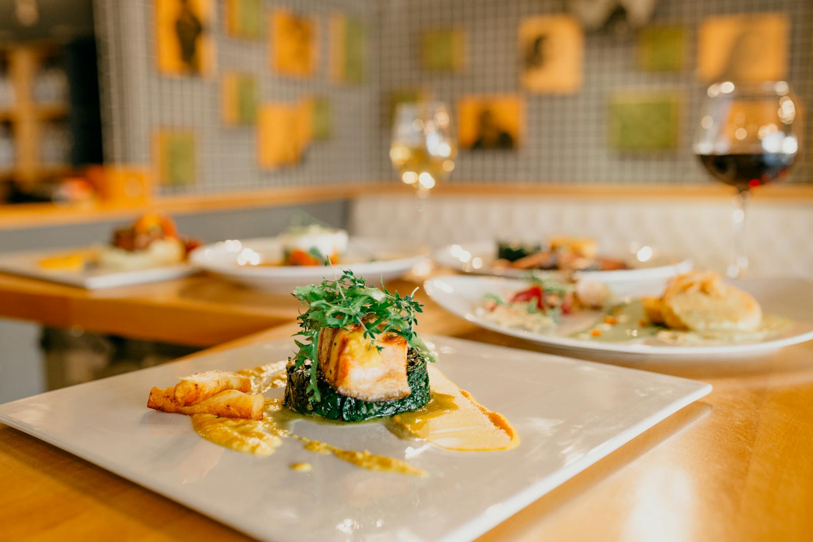 A spread of appetising dishes and glasses of wine on a wooden table in a bright modern restaurant