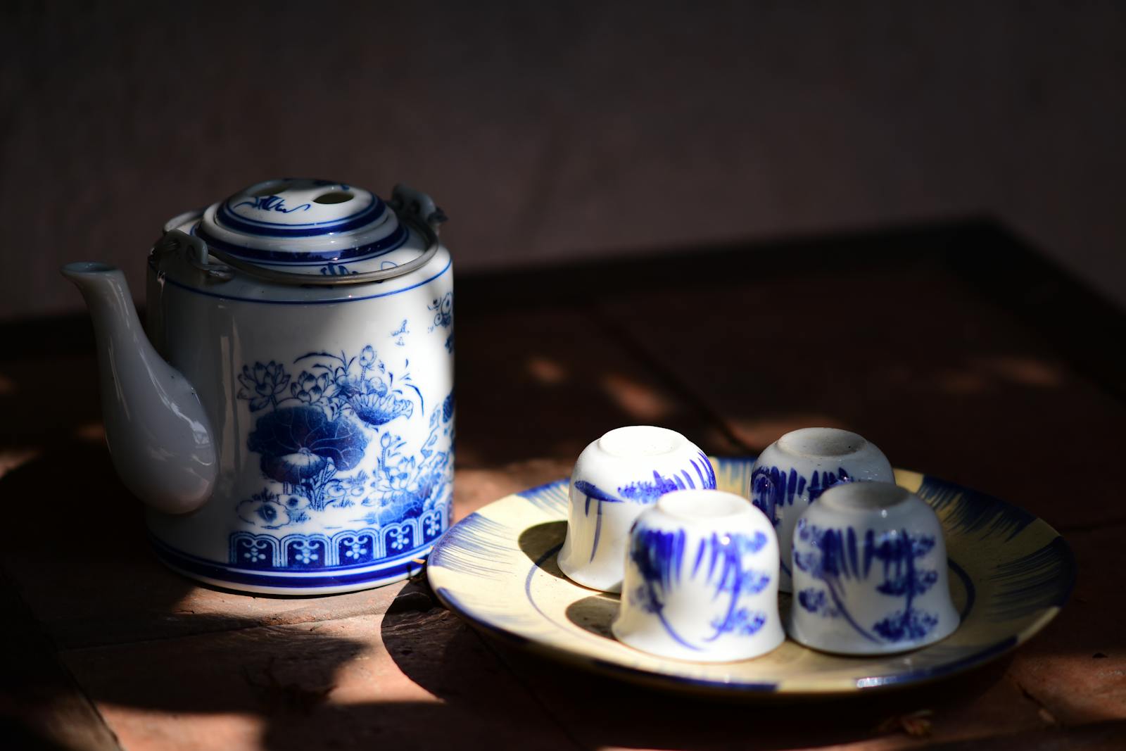 An elegant vintage blue and white teapot with matching cups on a wooden table