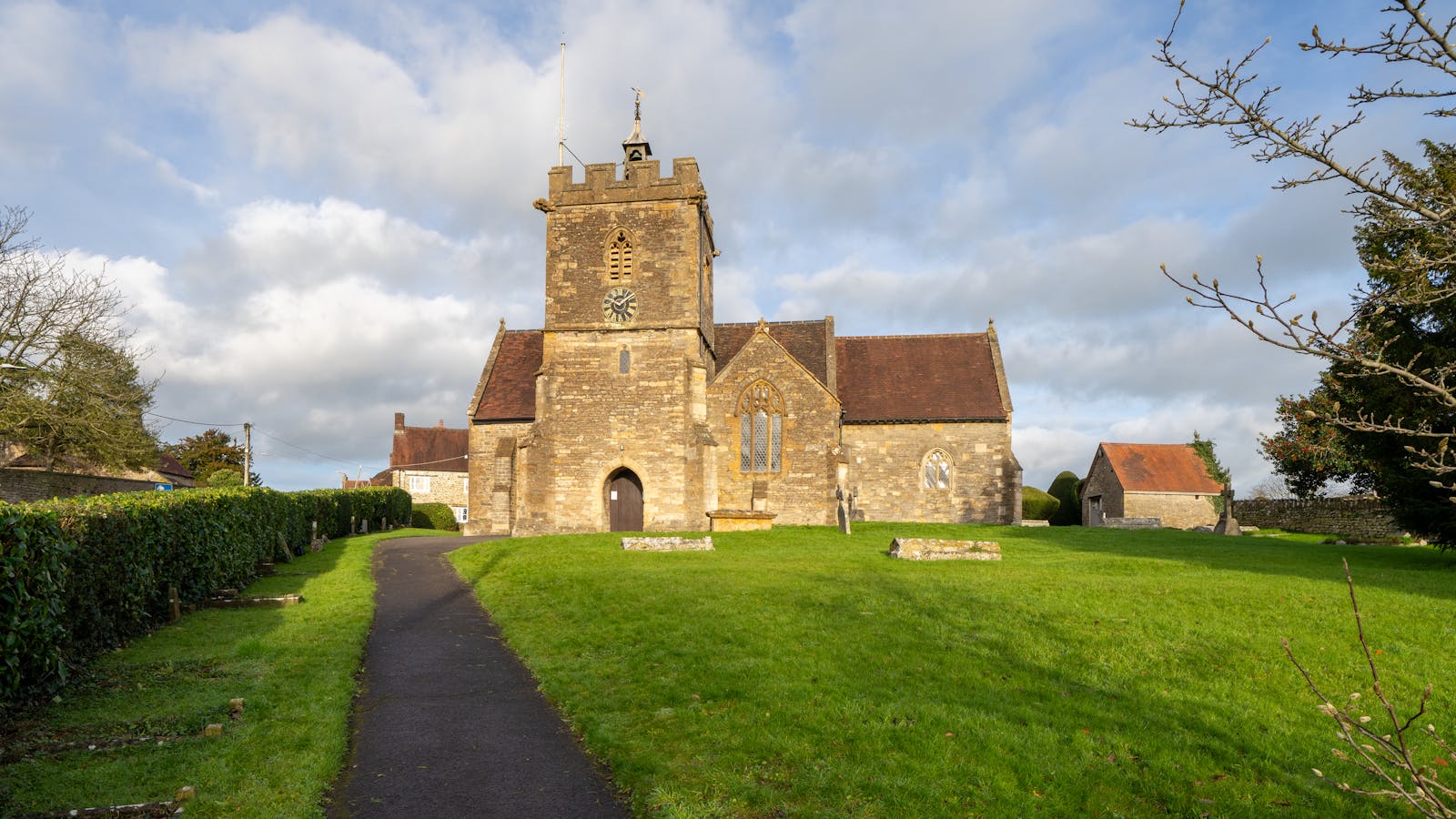 A historic English stone church with a bell tower surrounded by greenery