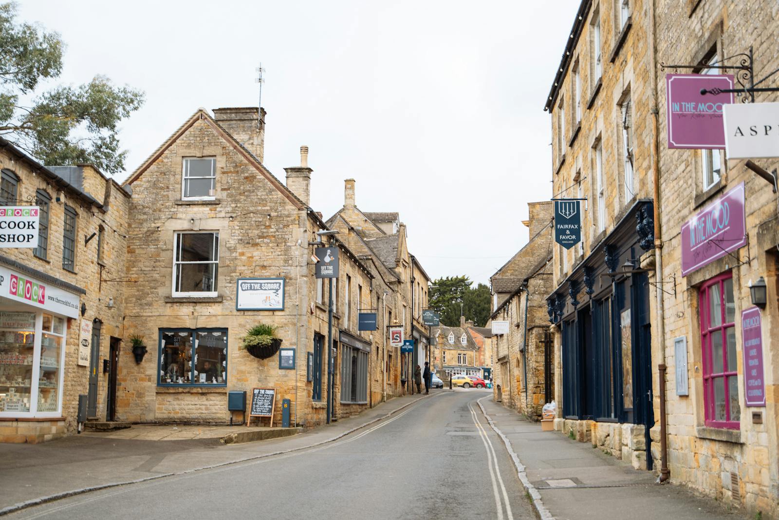 A picturesque honey-stone Cotswold village street lined with shops, a popular base for a stay