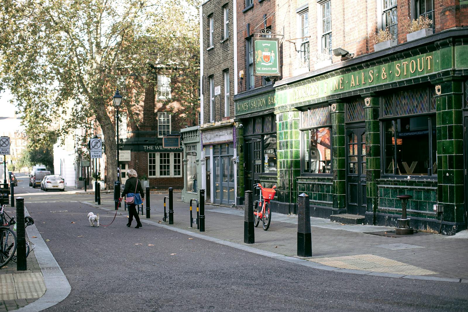 A person walking a dog past a traditional pub on a quiet street