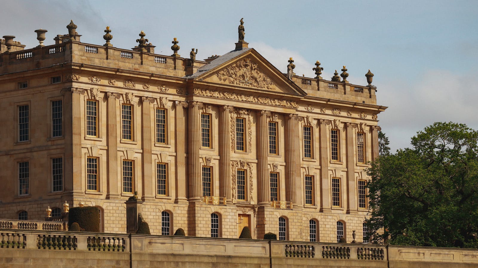 A grand historic English country house of pale stone under a bright sky