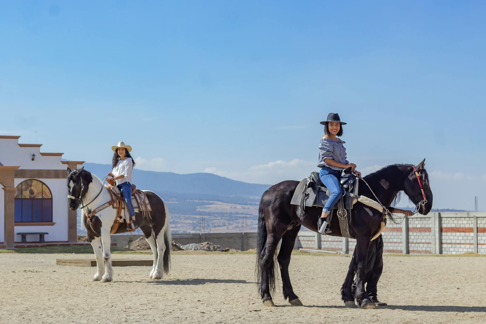 Two riders on horseback crossing open countryside on a clear, sunny day