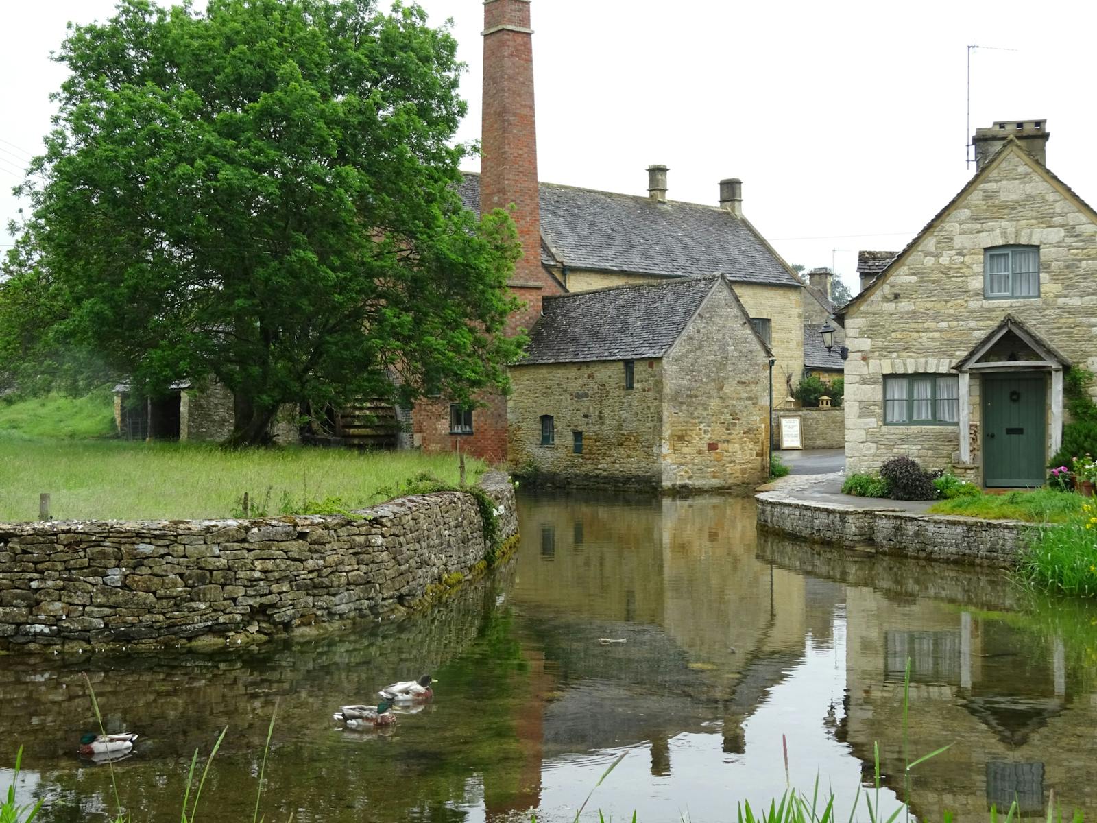 A historic Cotswold stone mill reflected in a still village pond