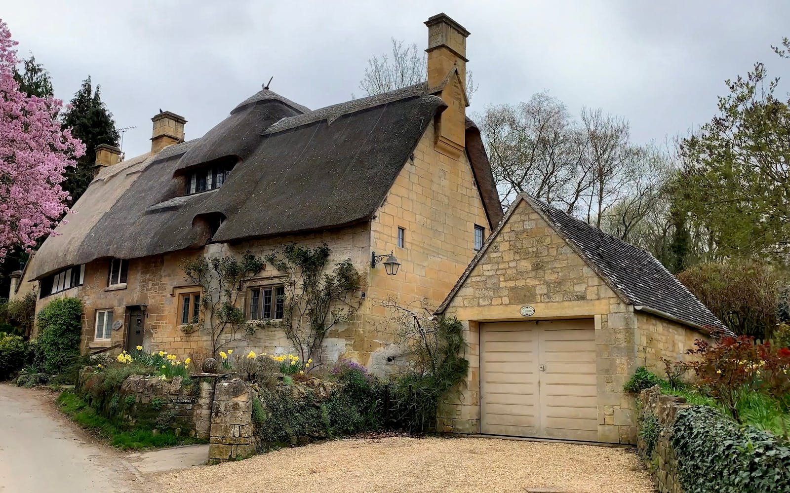 Honey-coloured thatched stone cottage in Stanton village in the Cotswolds, framed by spring blossom