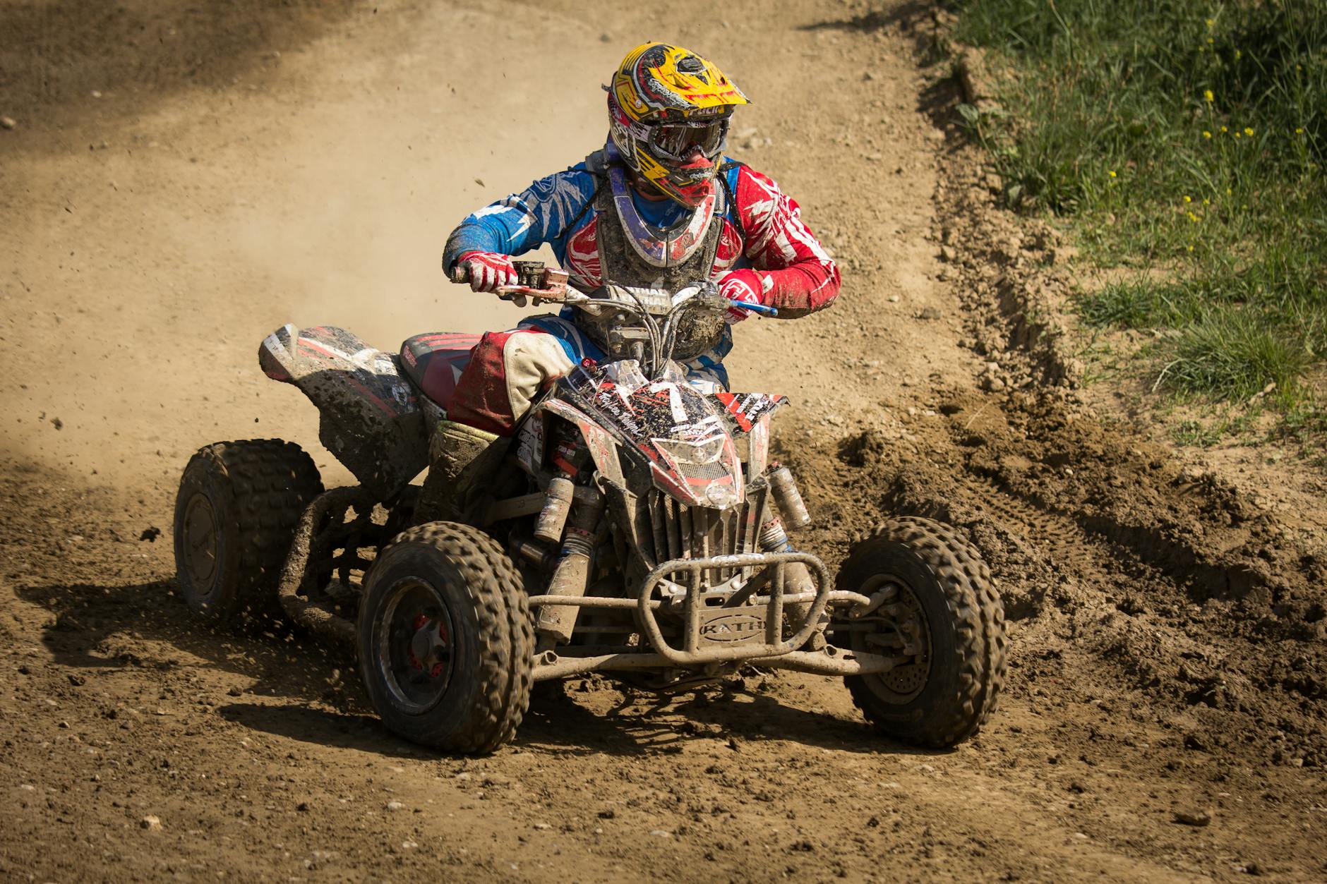 A helmeted rider on a quad bike speeding through a muddy off-road track