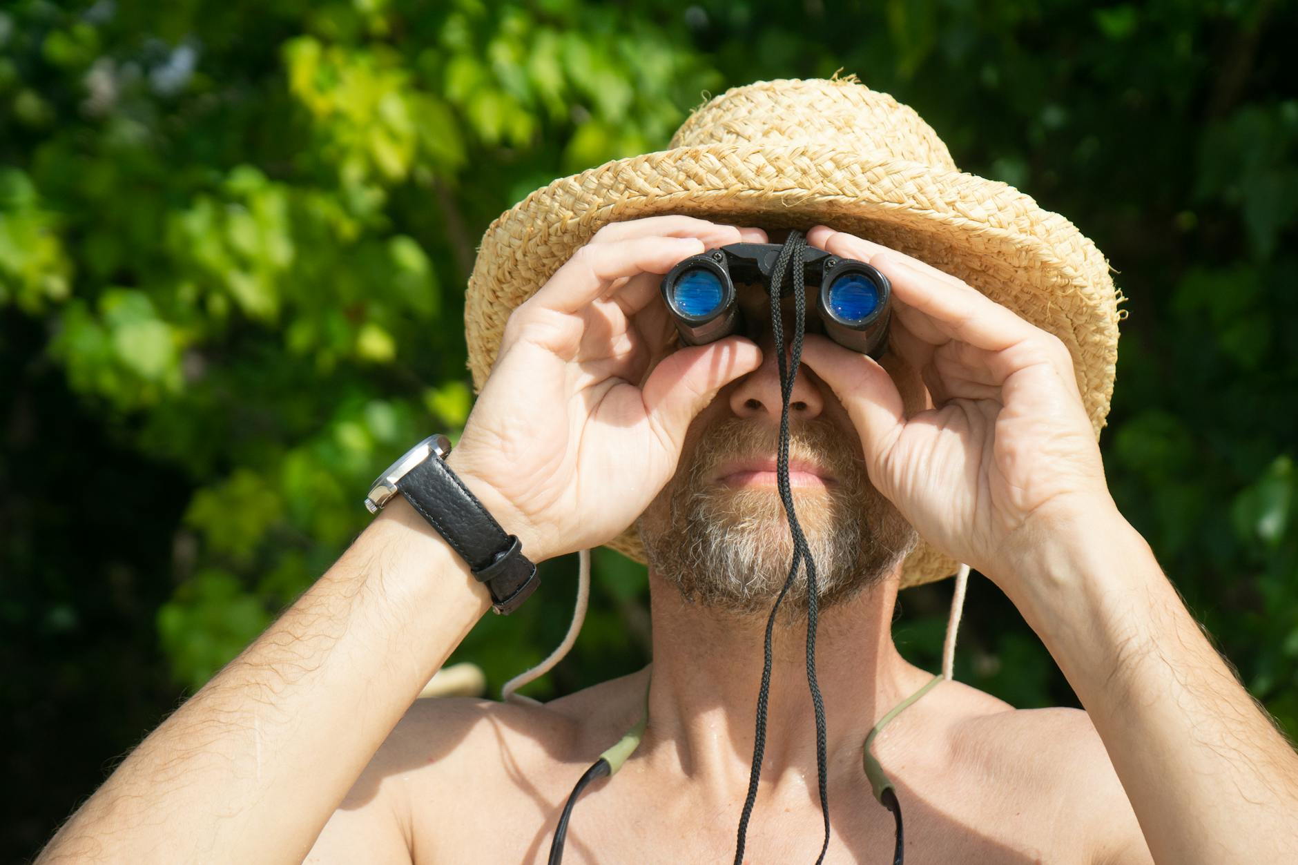 A birdwatcher in a straw hat looking through binoculars in a green landscape