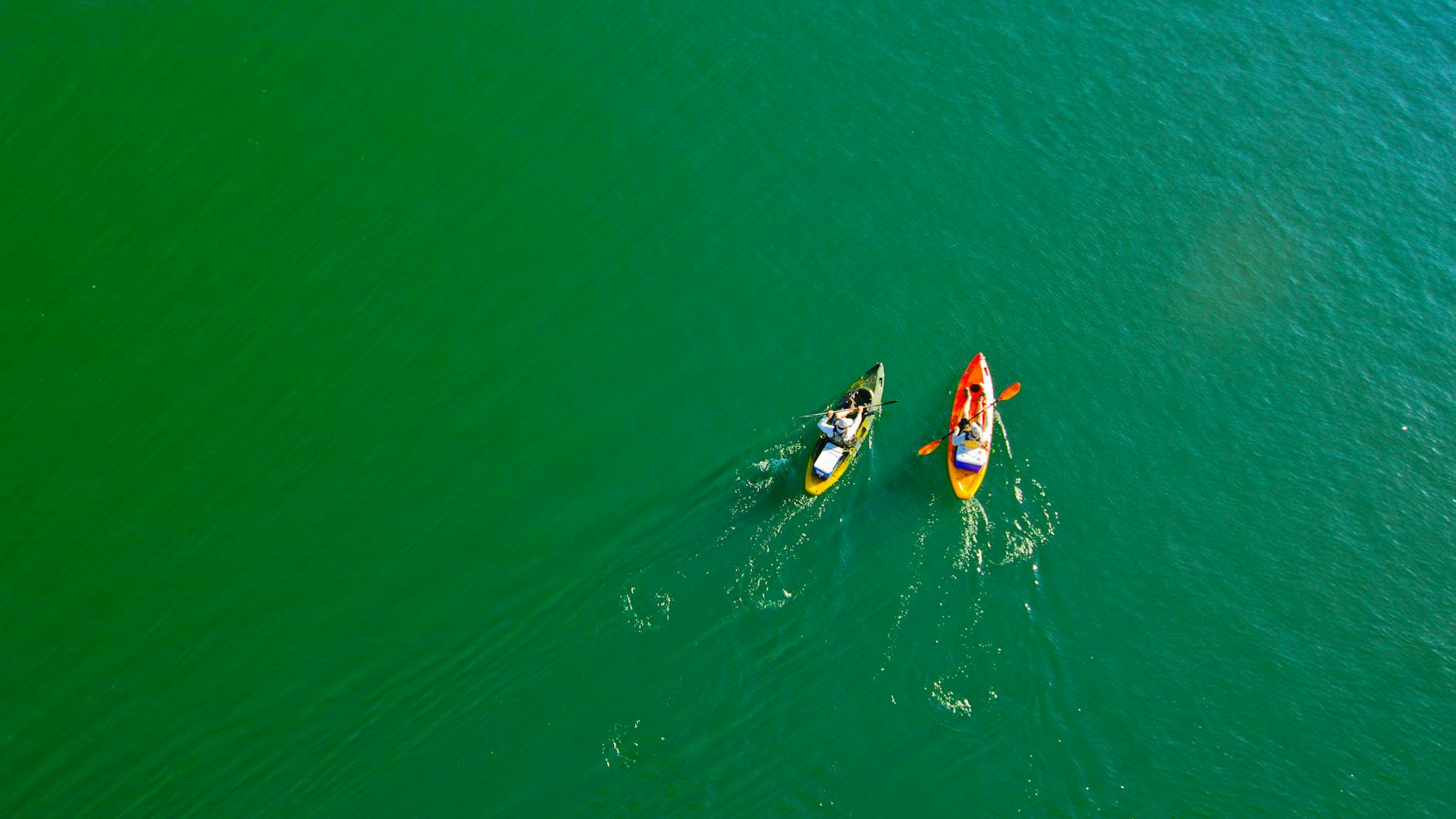 Two colourful kayaks being paddled across a calm lake