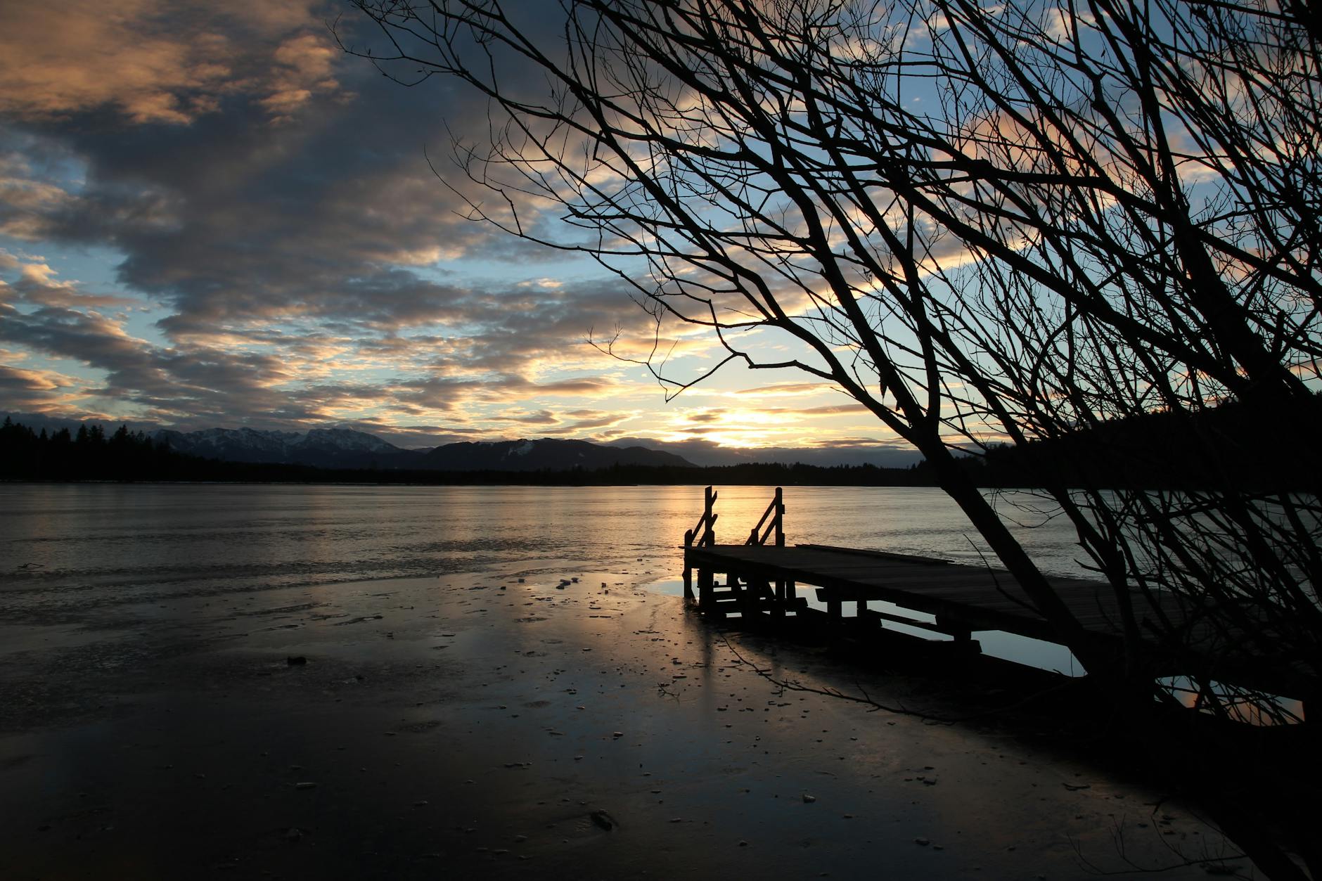 A tranquil sunset over a lake at Cotswold Lakes with a jetty silhouette