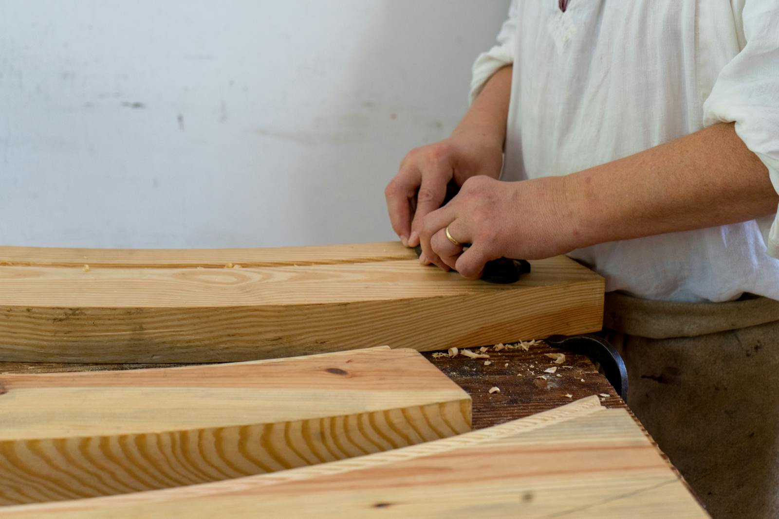 A craftsman shaping wood by hand in a workshop, in the Cotswolds Arts and Crafts tradition