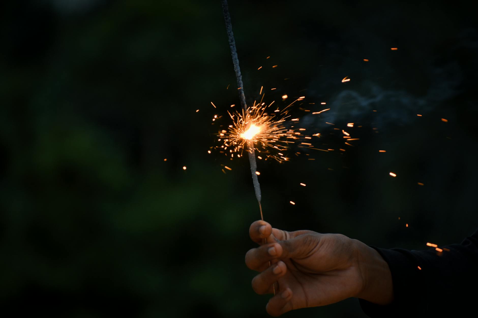 A hand holding a lit sparkler creating a shower of sparks at night