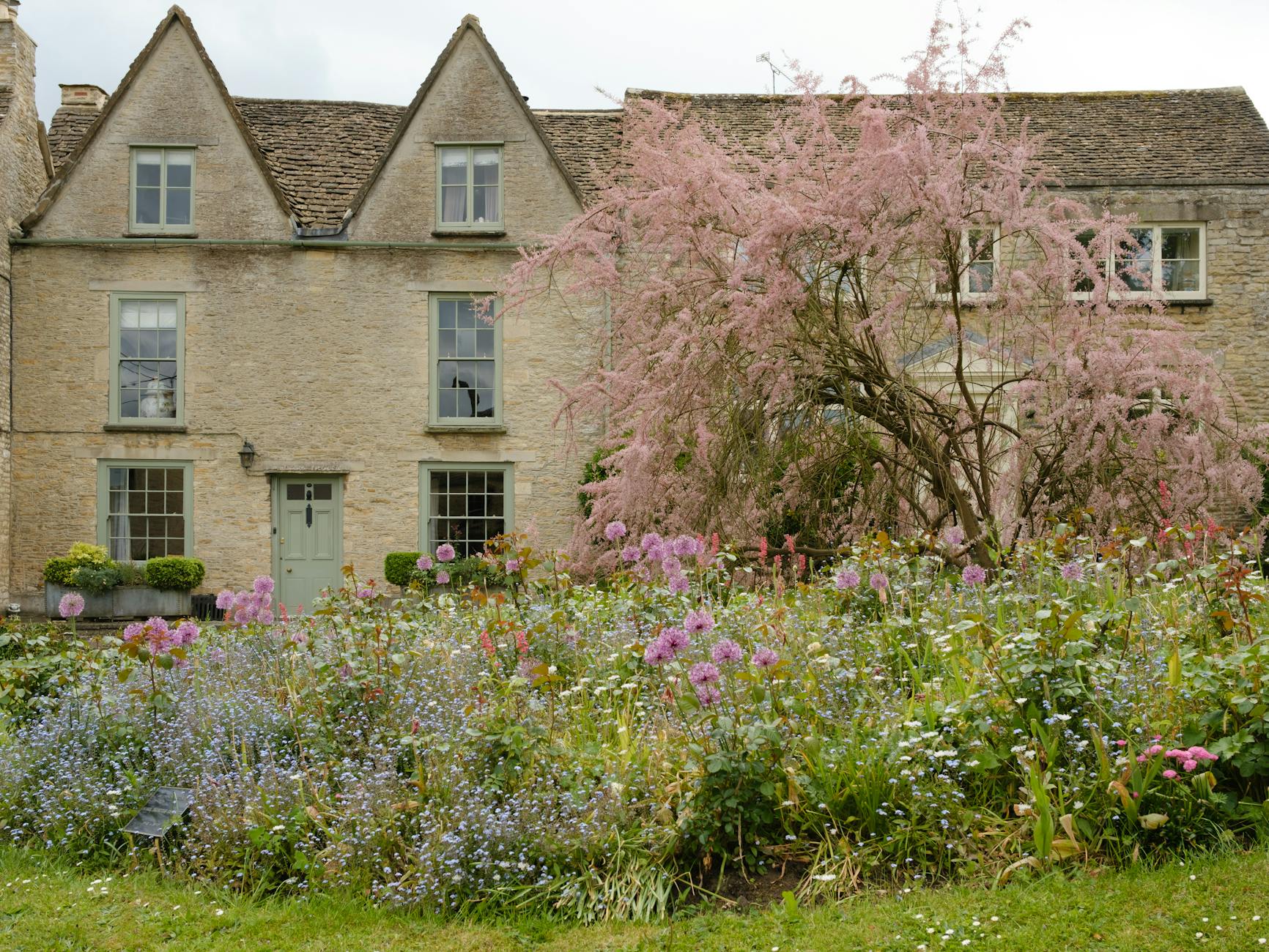 A honey-coloured Cotswold stone cottage with a lush flower-filled garden