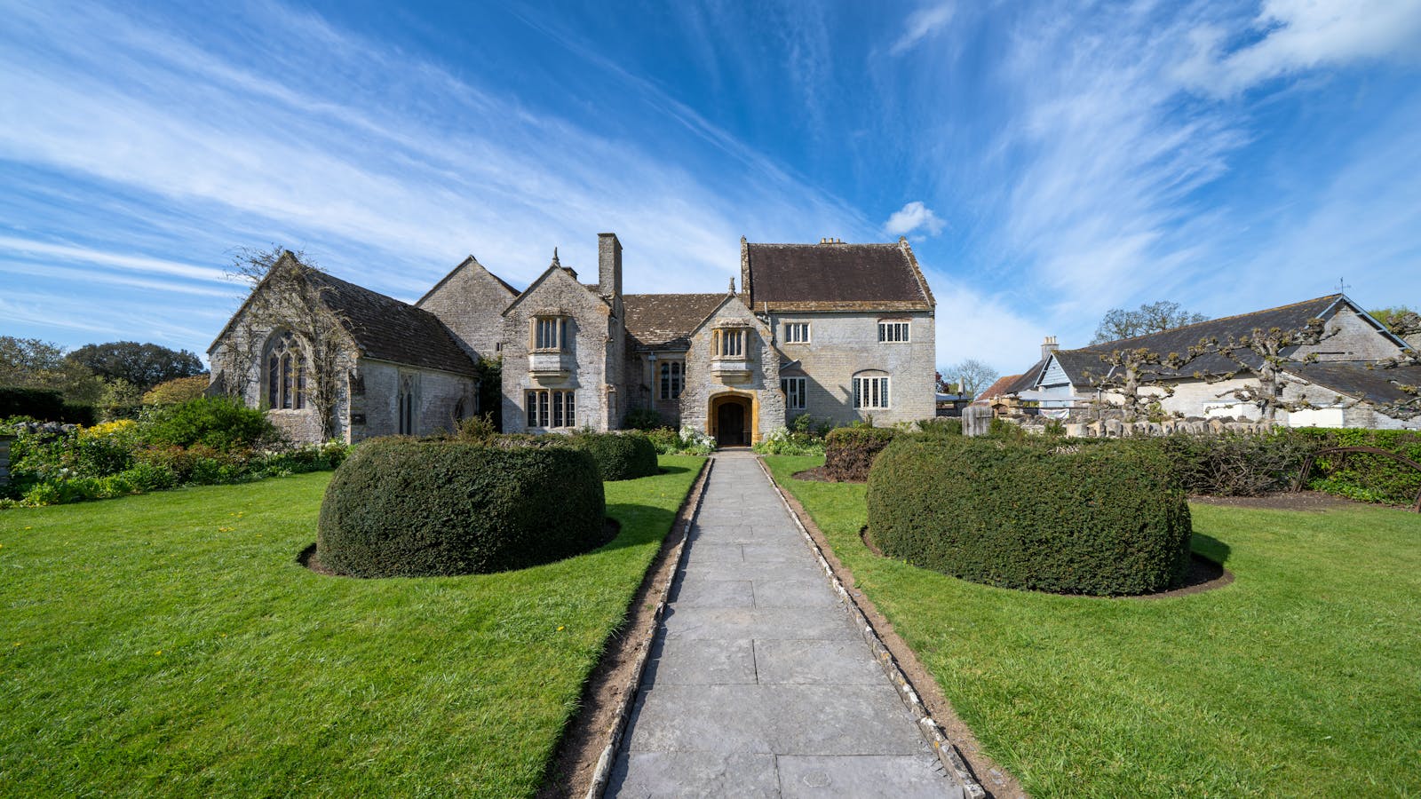 A grand historic English country house surrounded by lush gardens in the Cotswolds
