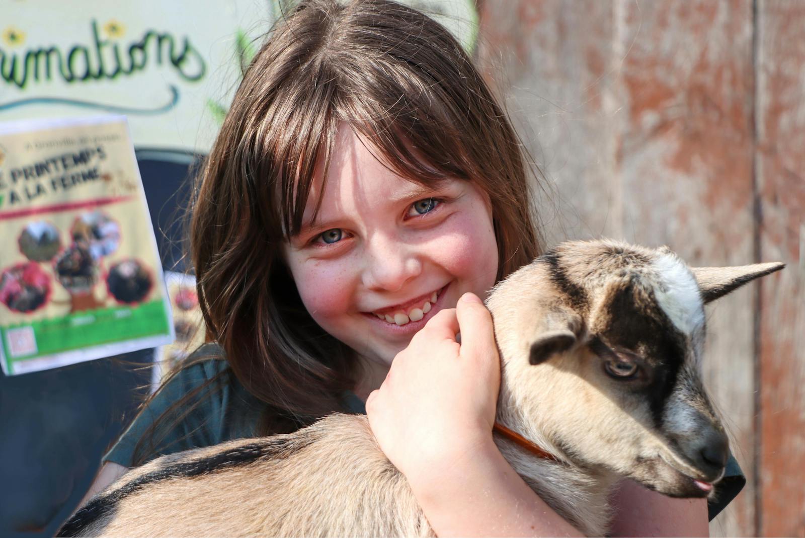 A smiling girl cuddling a baby goat at a Cotswolds farm park