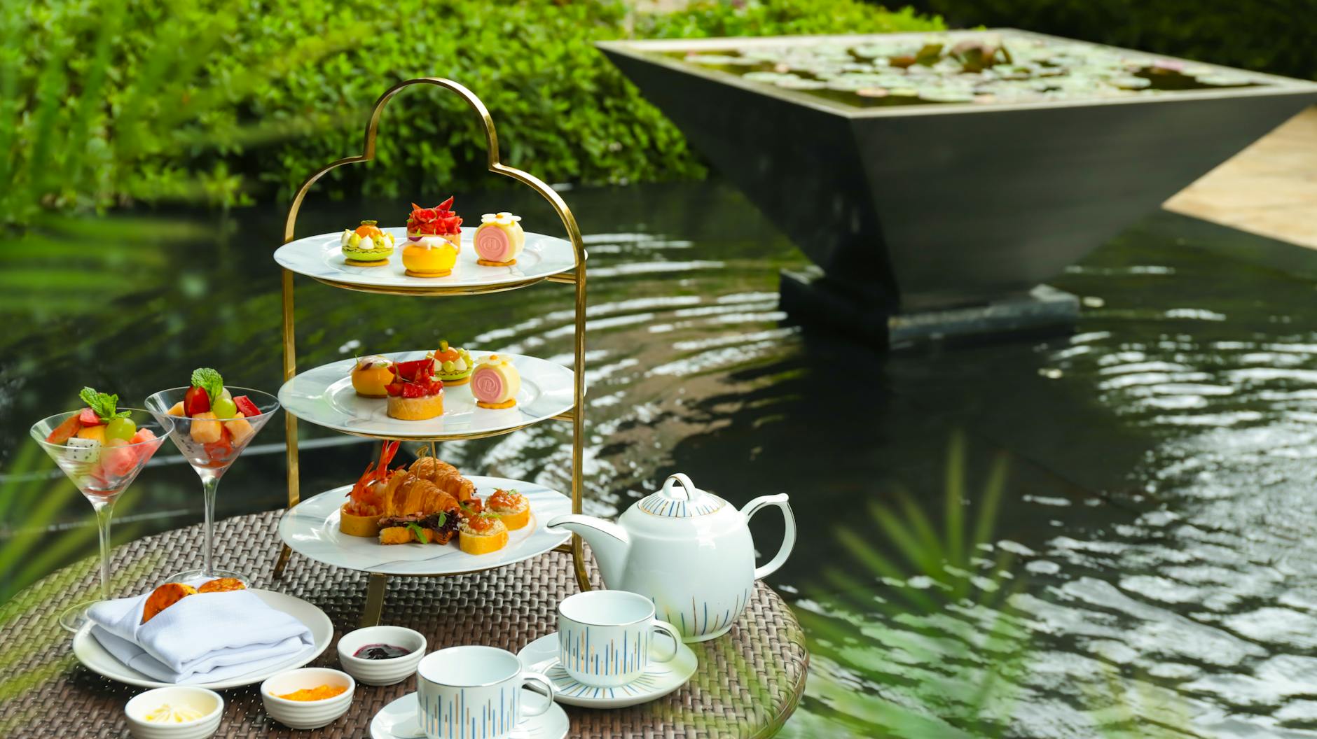 An afternoon tea setup with cakes and a teapot beside a garden