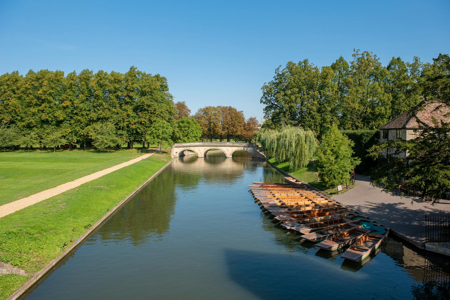 A stone bridge and boats on a river in a lush green Cotswold village in summer