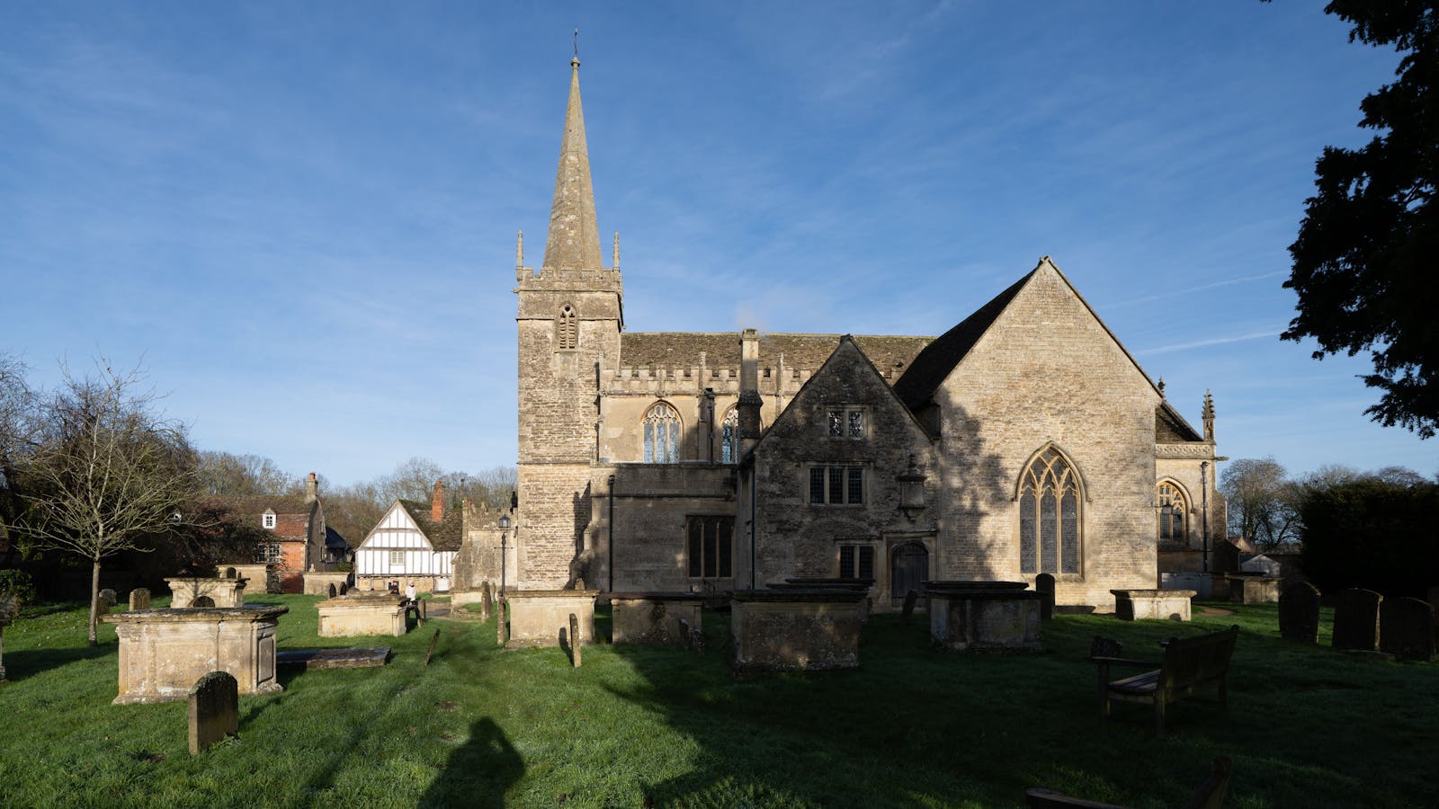 A grand medieval stone wool church with a pinnacled tower under a blue Cotswold sky