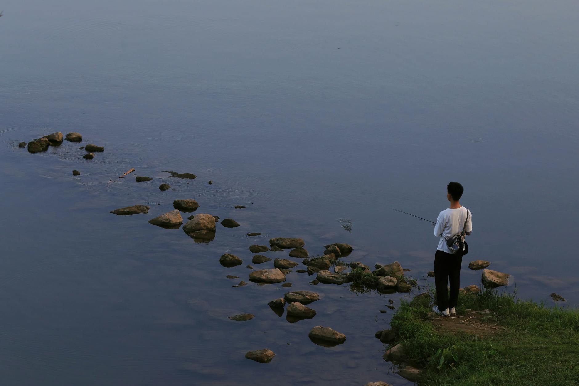 An angler fishing from the bank of a calm lake at dawn