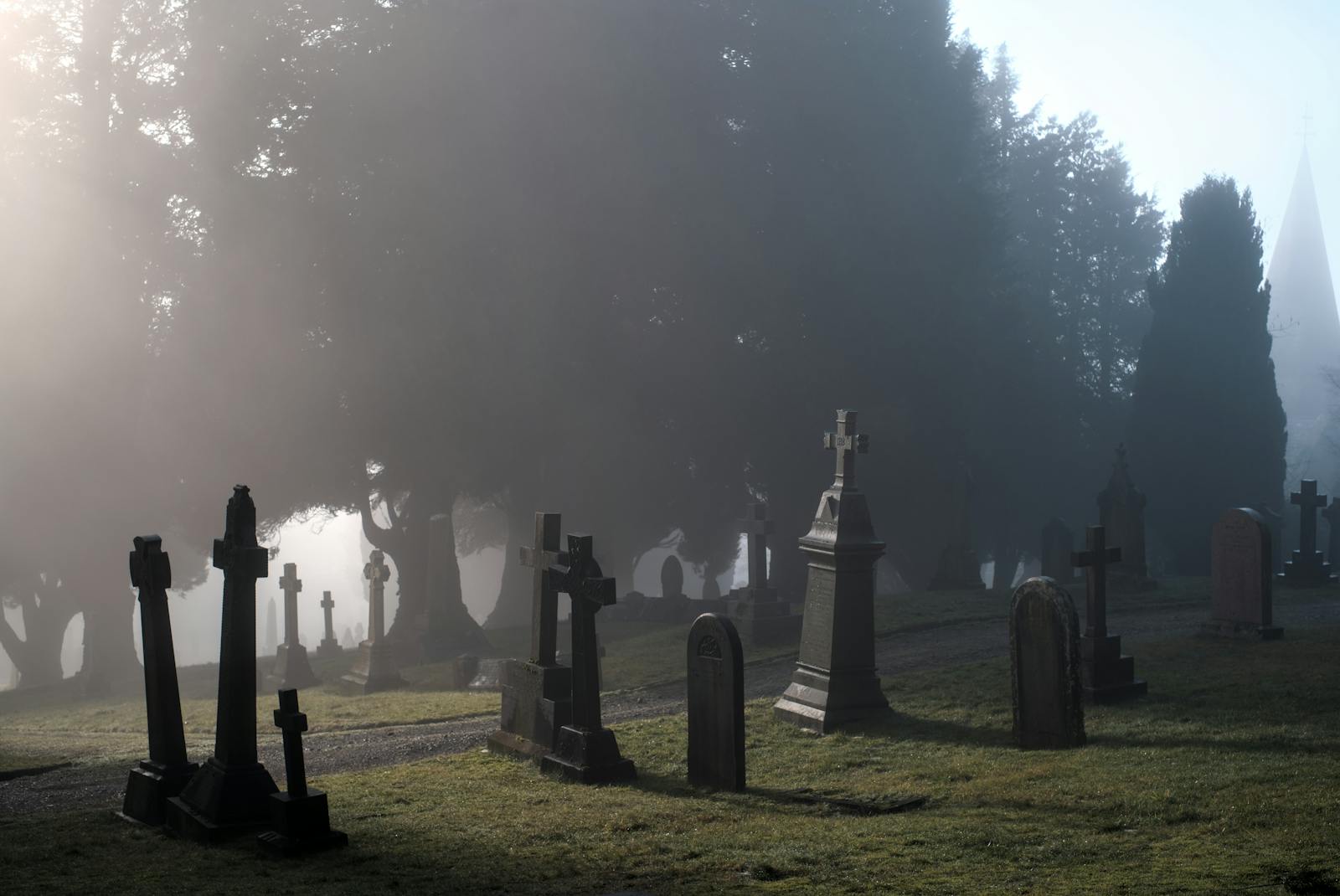 A misty graveyard with old gravestones and bare trees on a foggy morning in England