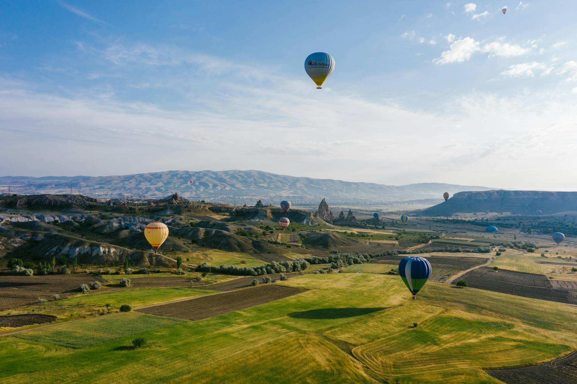 Colourful hot air balloons floating over a patchwork of green countryside fields