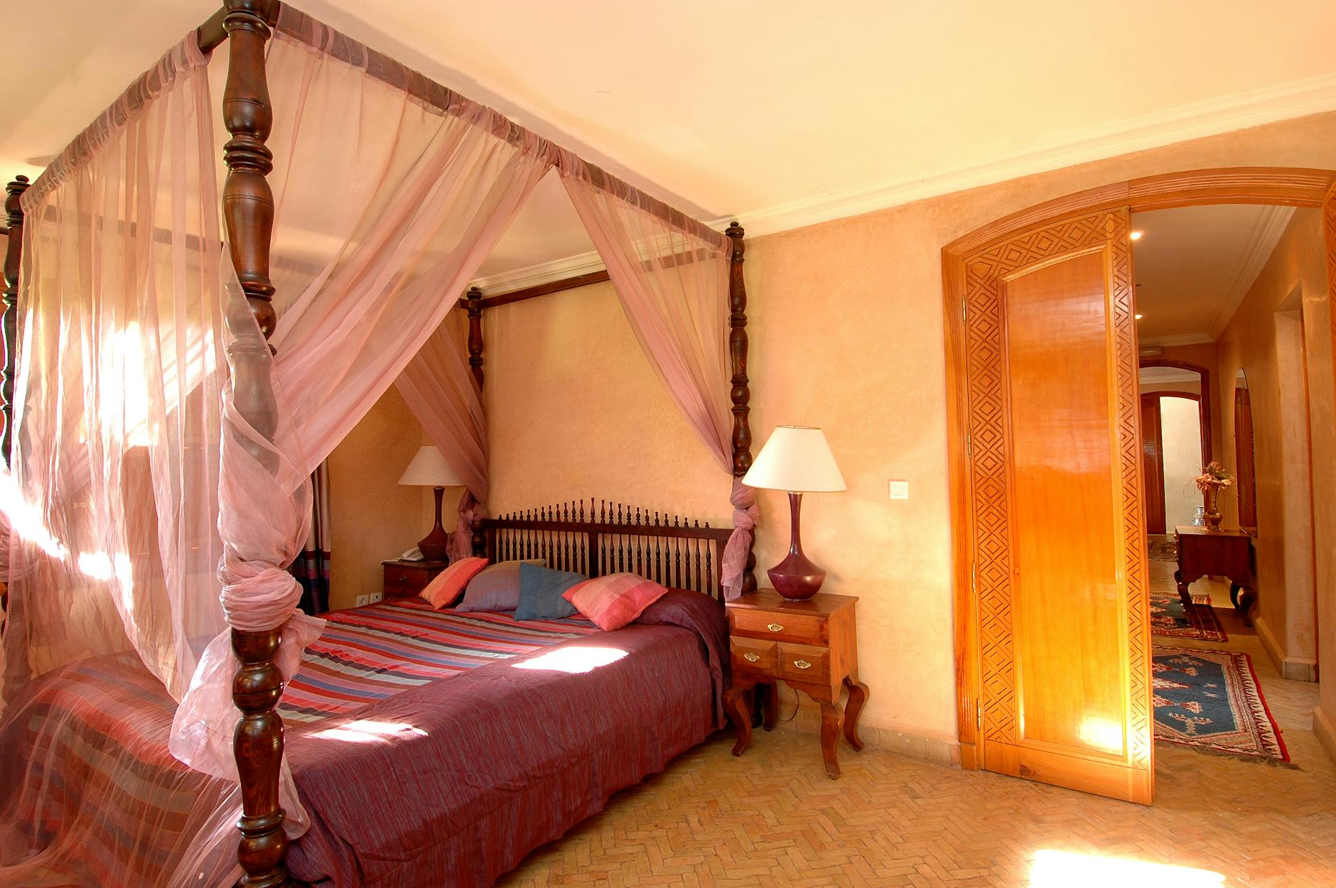 An elegant hotel bedroom with a four-poster canopy bed and soft romantic lighting