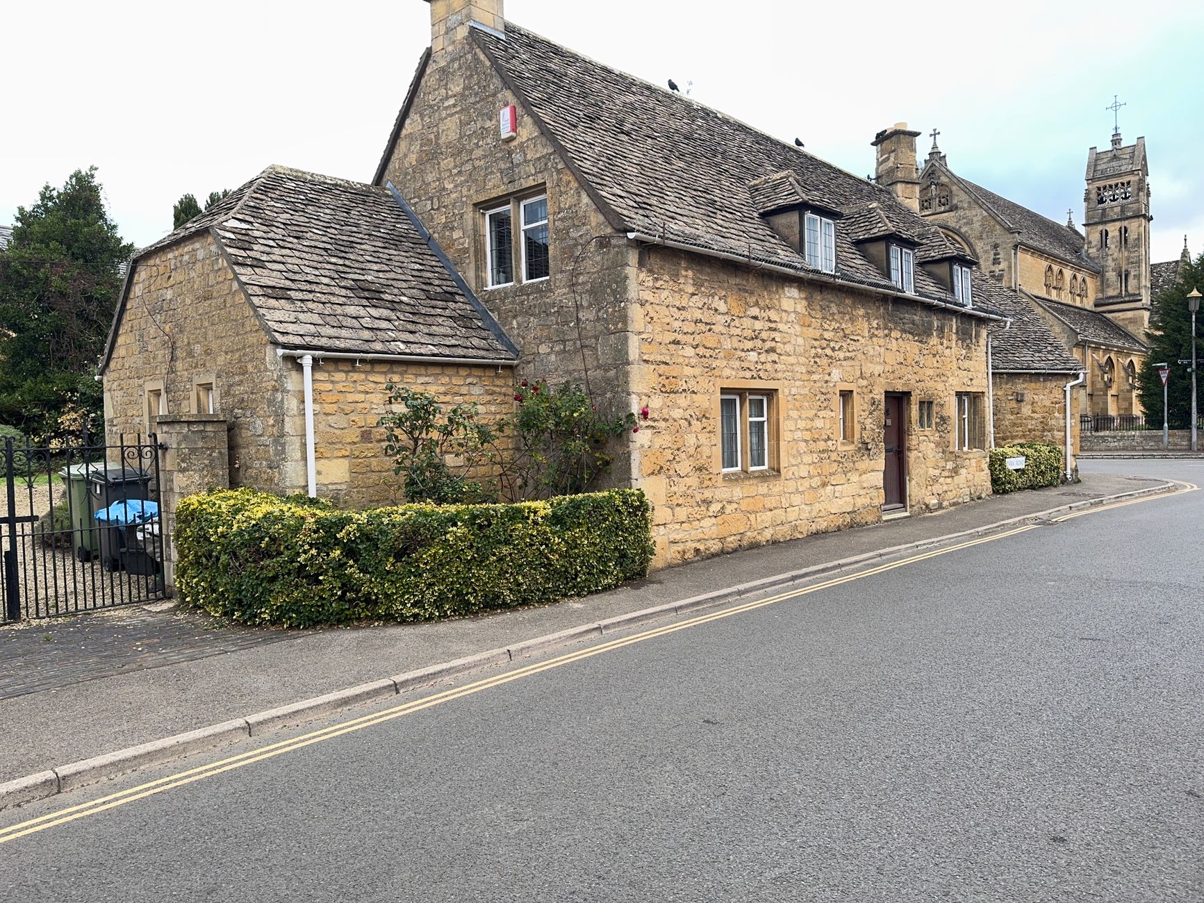 Pale Cotswold stone cottage with a church tower behind in Stow-on-the-Wold