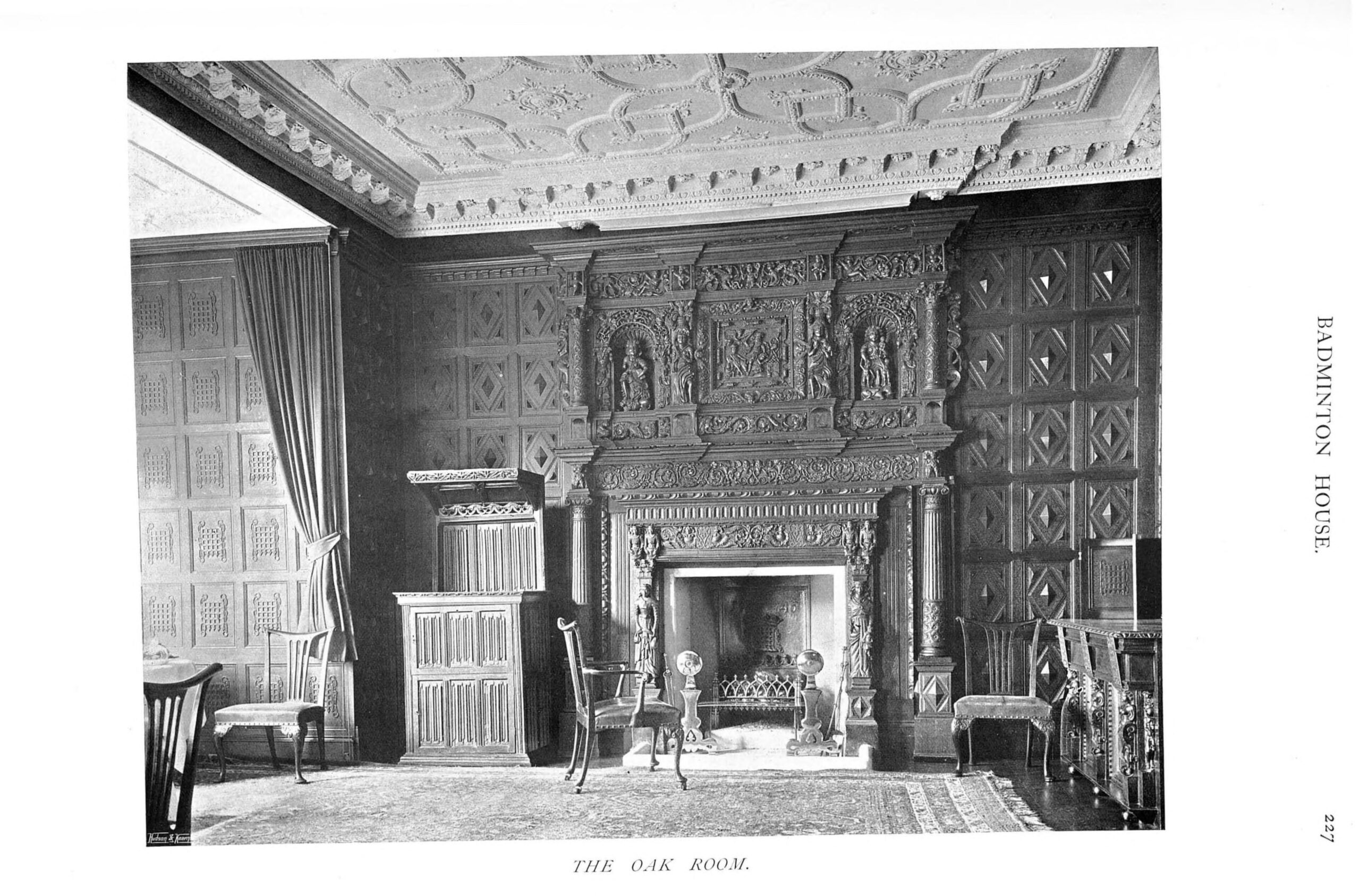 An early twentieth-century black-and-white photograph of the Oak Room at Badminton House, with a heavily carved oak chimneypiece, diamond-pattern panelling and an ornate plaster ceiling