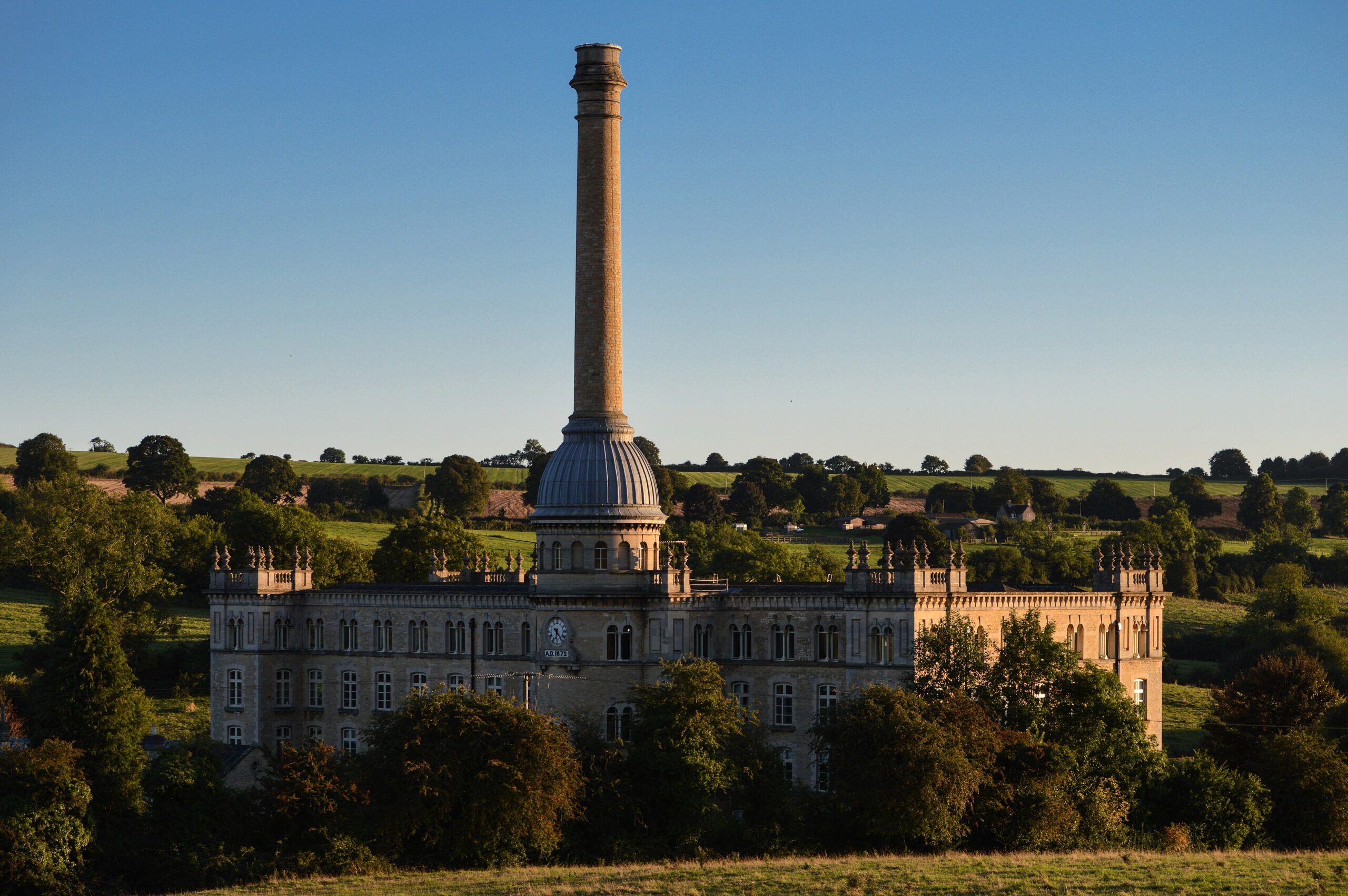 Bliss Tweed Mill at Chipping Norton in evening light, its domed chimney rising above a battlemented stone mill building