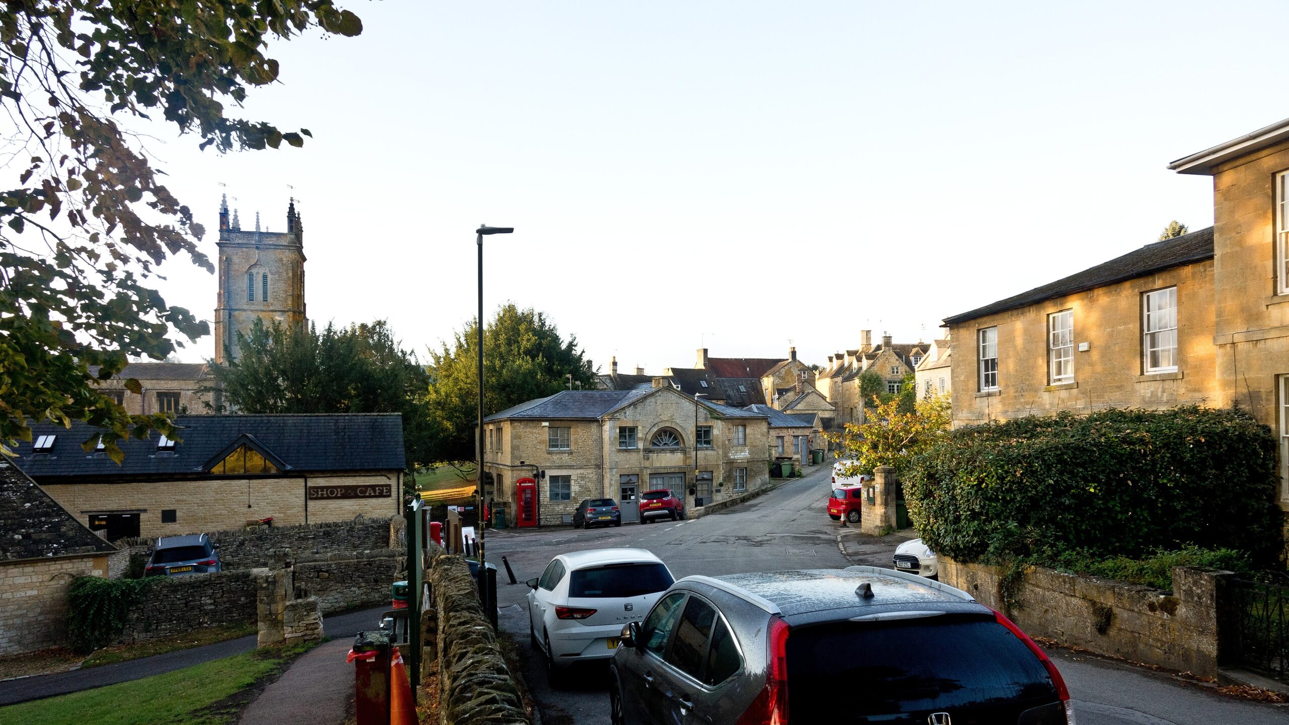 The village square in Blockley with honey-coloured stone houses, a red phone box and the pinnacled tower of the Church of St Peter and St Paul