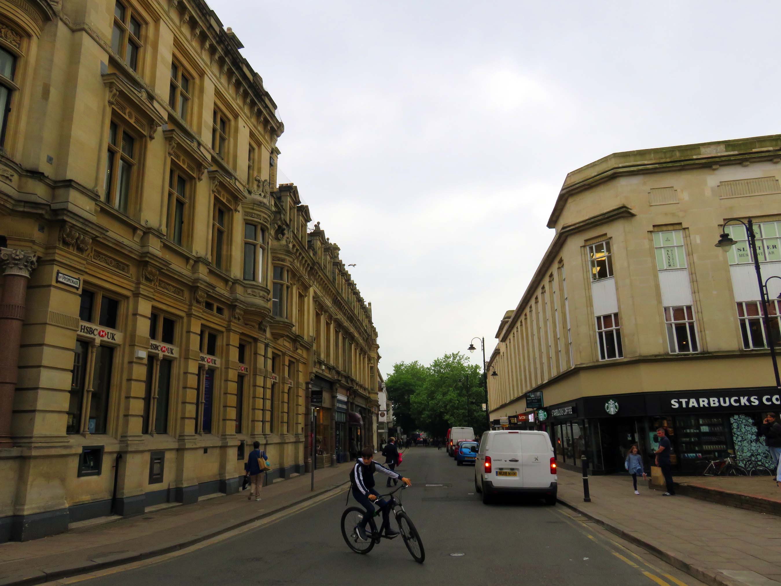 The Promenade in Cheltenham with Regency stone frontages, shops and a cyclist on the road