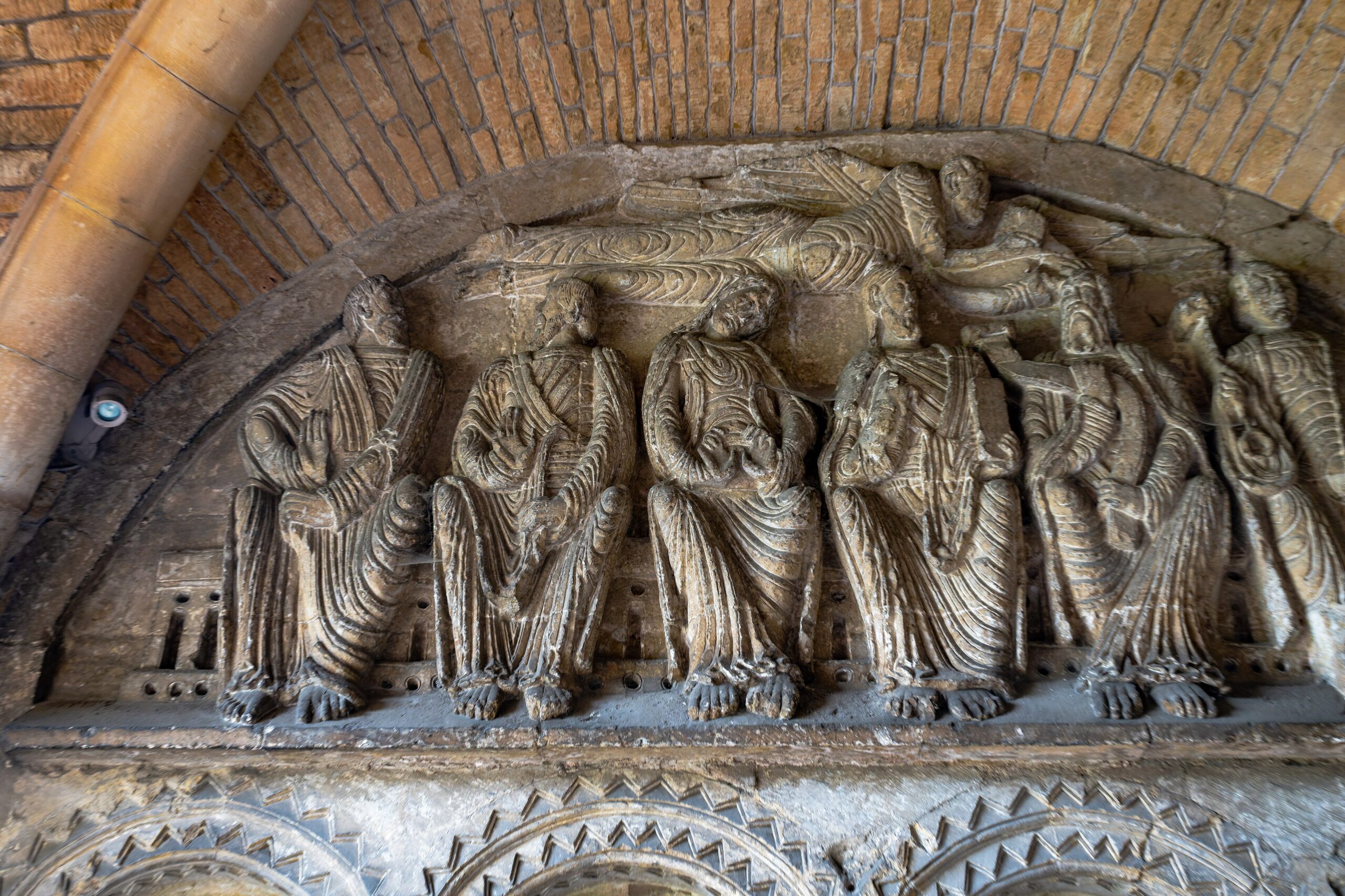 The Romanesque tympanum in the south porch of Malmesbury Abbey showing seated apostles in deeply carved drapery beneath a flying angel