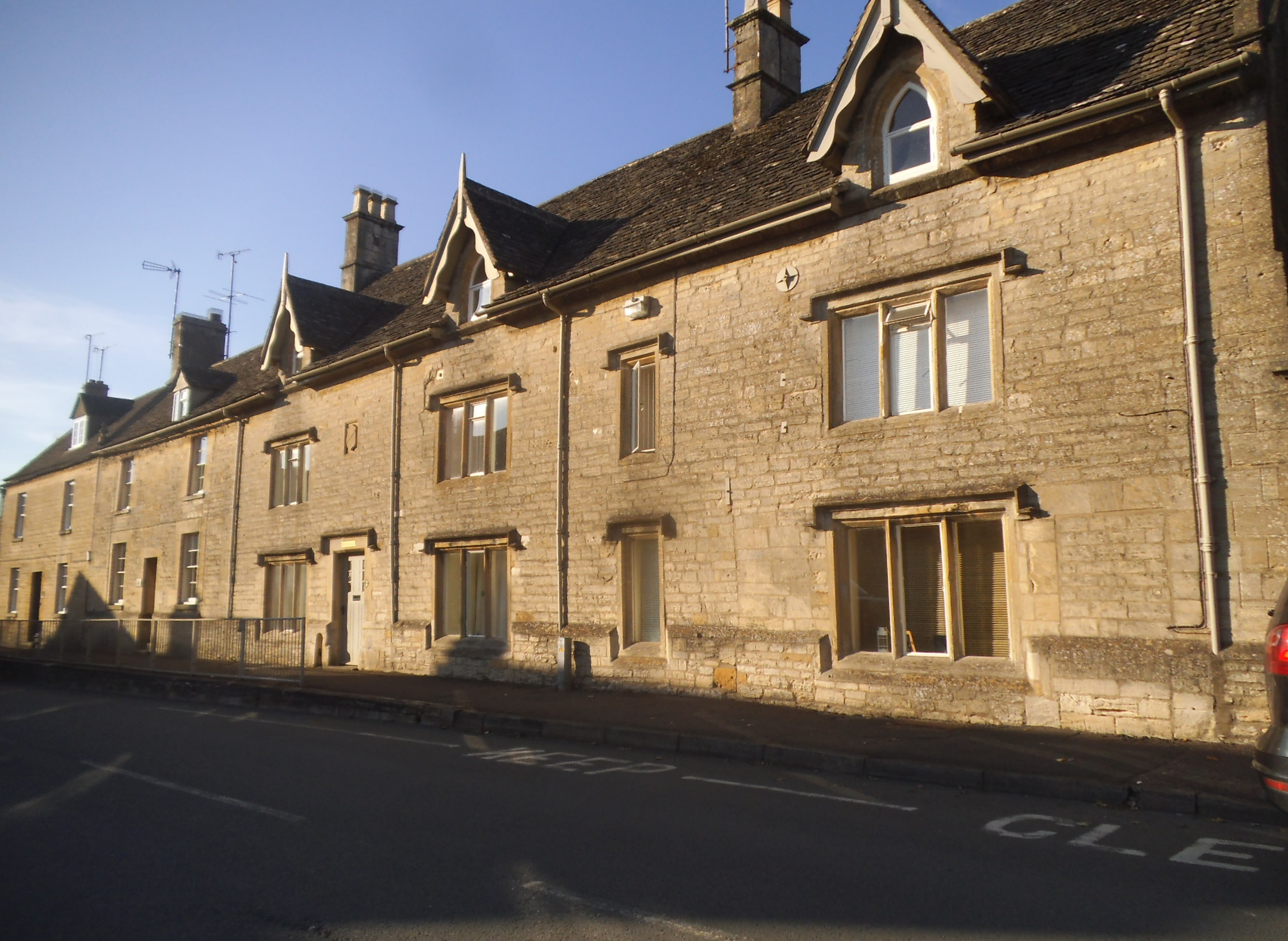 A row of honey-coloured Cotswold stone houses with gabled dormers on Northleach High Street in low golden light