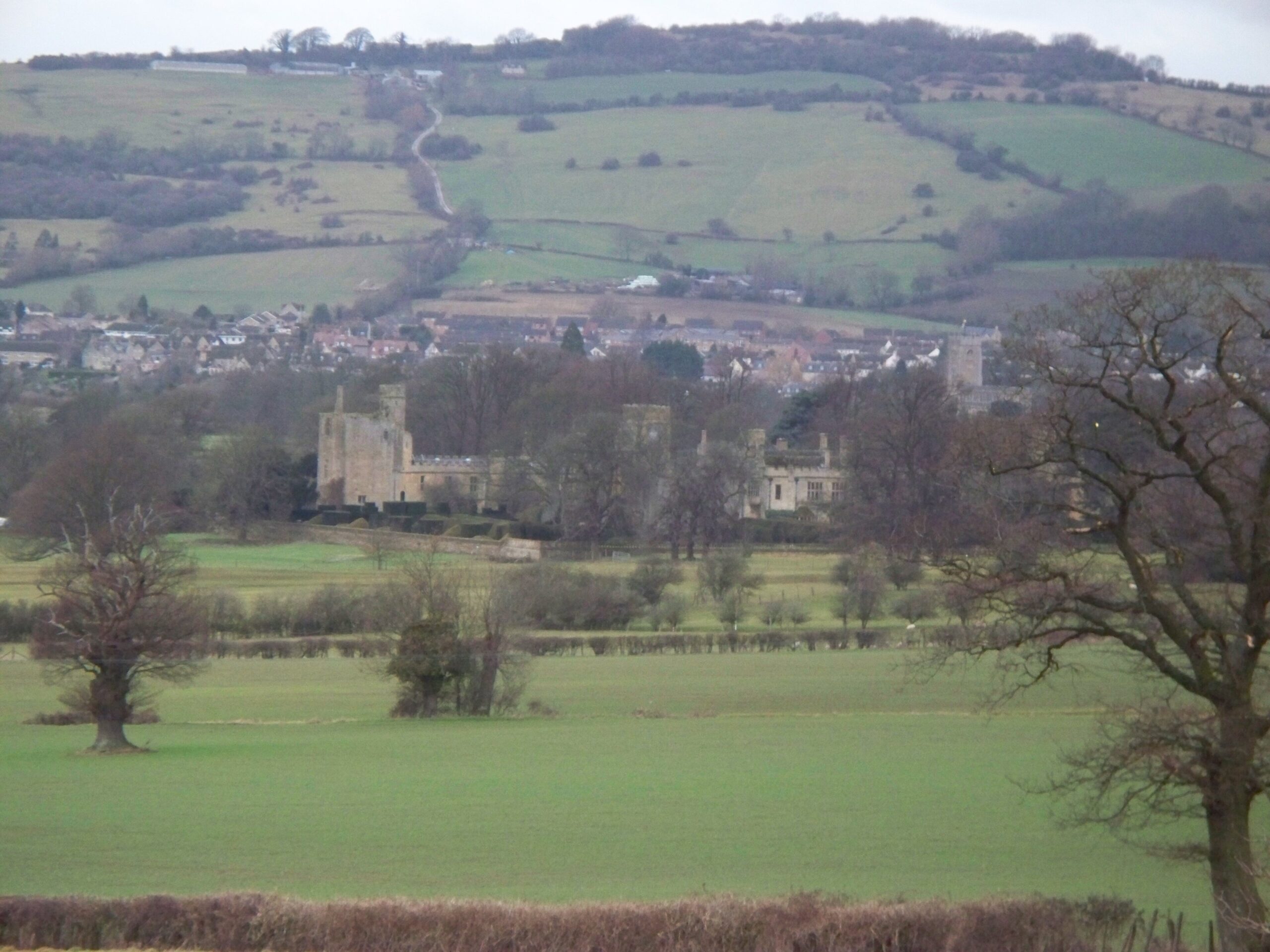 Sudeley Castle and its ruined banqueting hall in green fields below the Cotswold escarpment, with Winchcombe behind