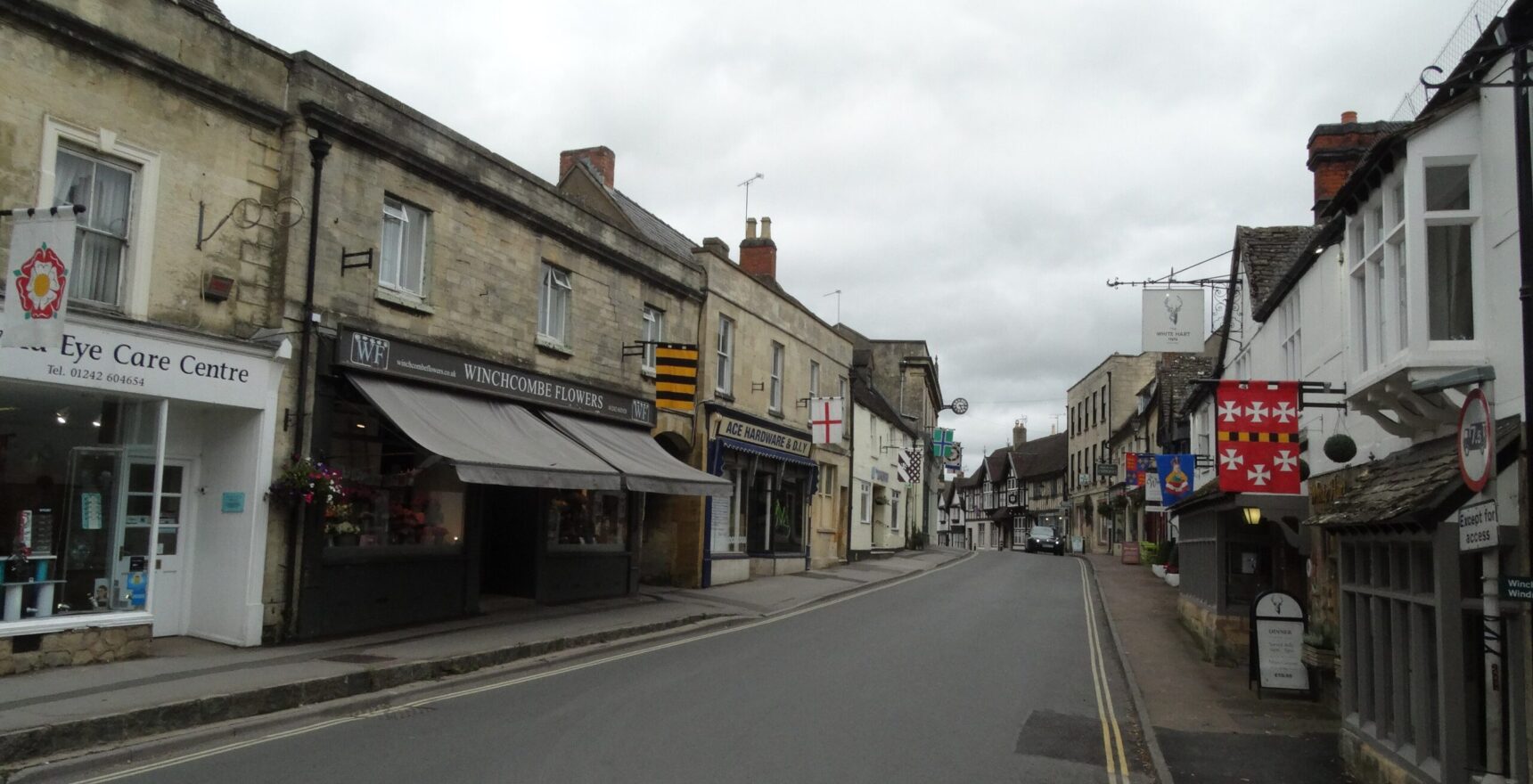 Winchcombe High Street with stone and timbered buildings, hanging pub signs and heraldic banners