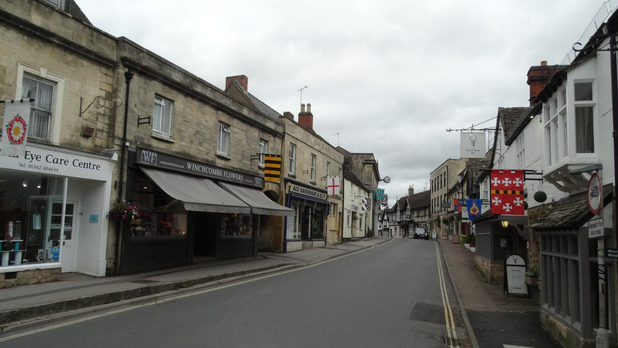 Winchcombe High Street with stone and timbered buildings, hanging pub signs and heraldic banners