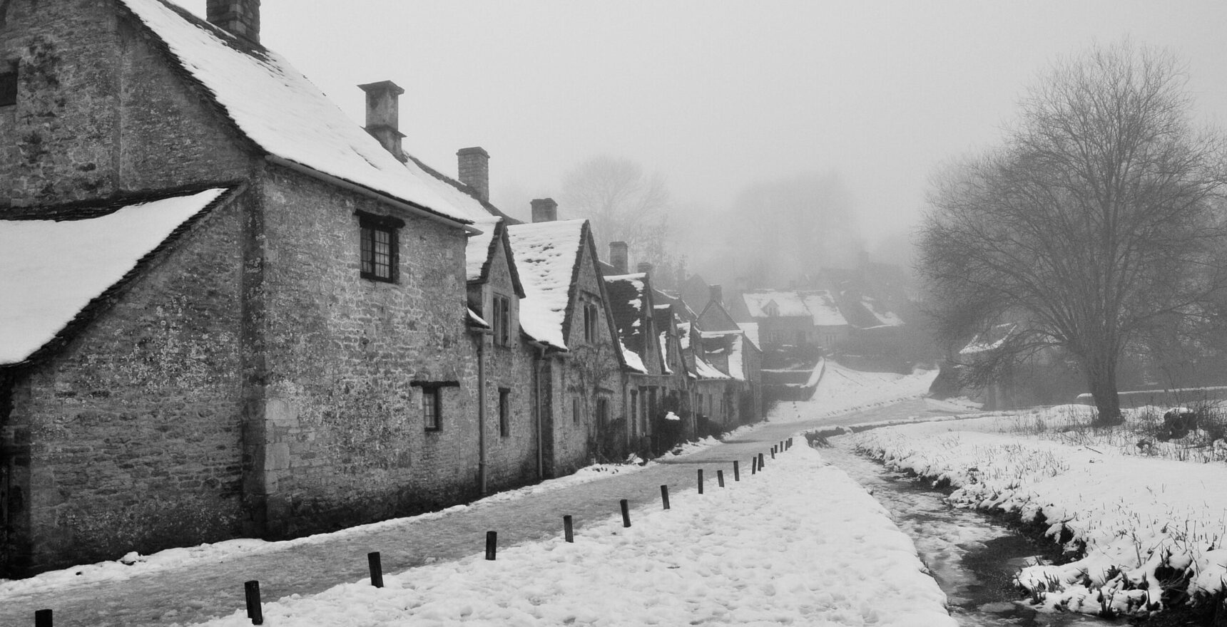 The cottages of Arlington Row in Bibury with snow on the roofs and the path, under a misty winter sky