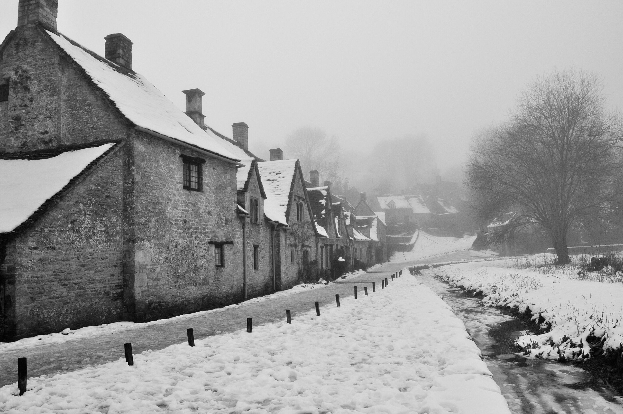 The cottages of Arlington Row in Bibury with snow on the roofs and the path, under a misty winter sky