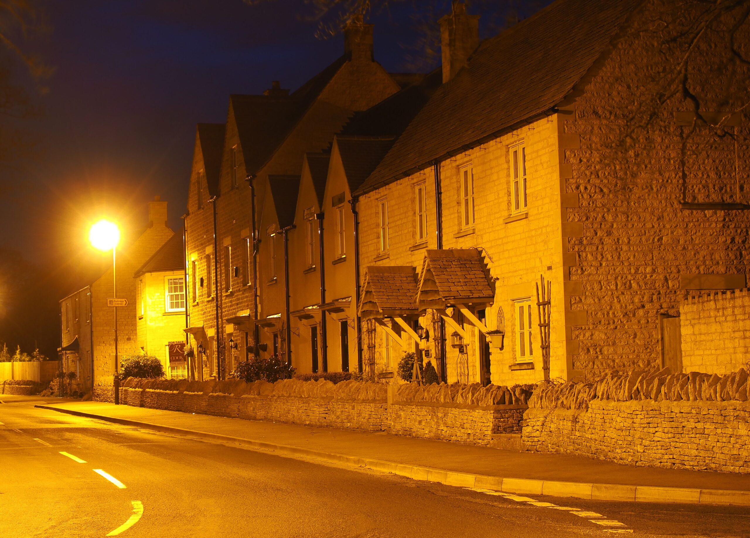 A terrace of stone houses lit orange by a street lamp at night in Birdlip, with a dark sky above