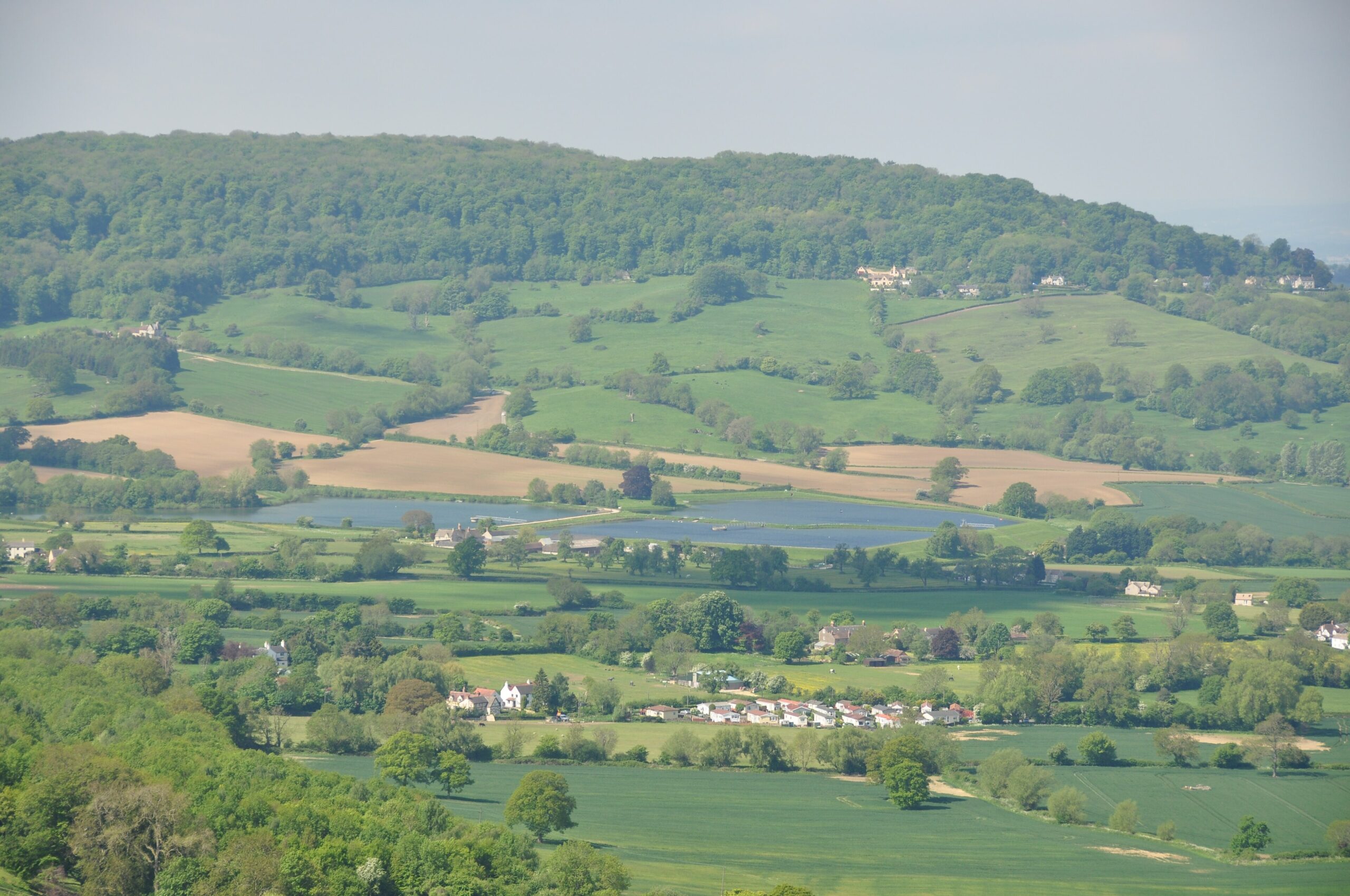 Looking across a patchwork of fields and small lakes in the vale to the long wooded ridge of Cooper's Hill, seen from Crickley Hill