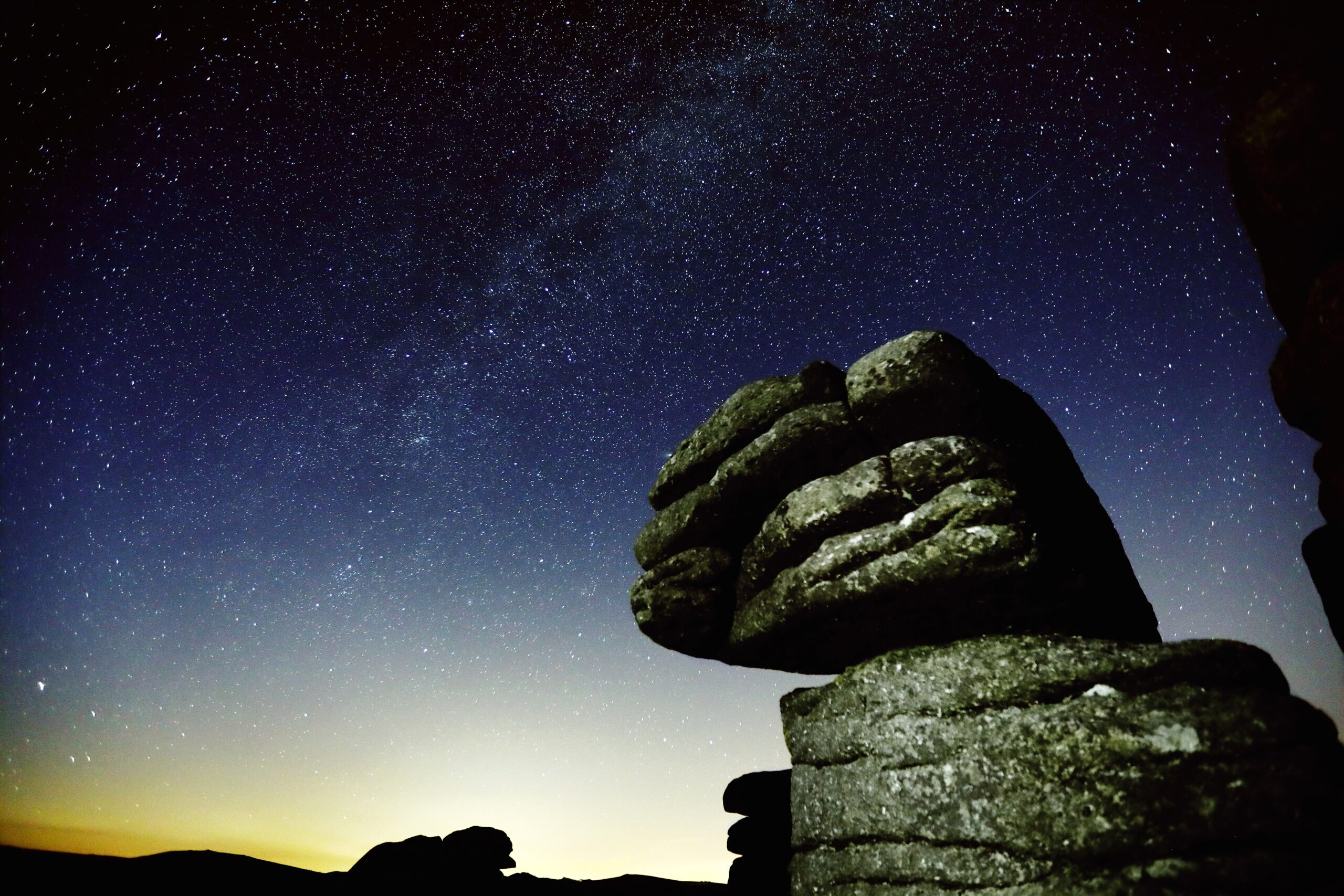 The Milky Way arching across a star-filled sky above a granite tor at dusk on Dartmoor