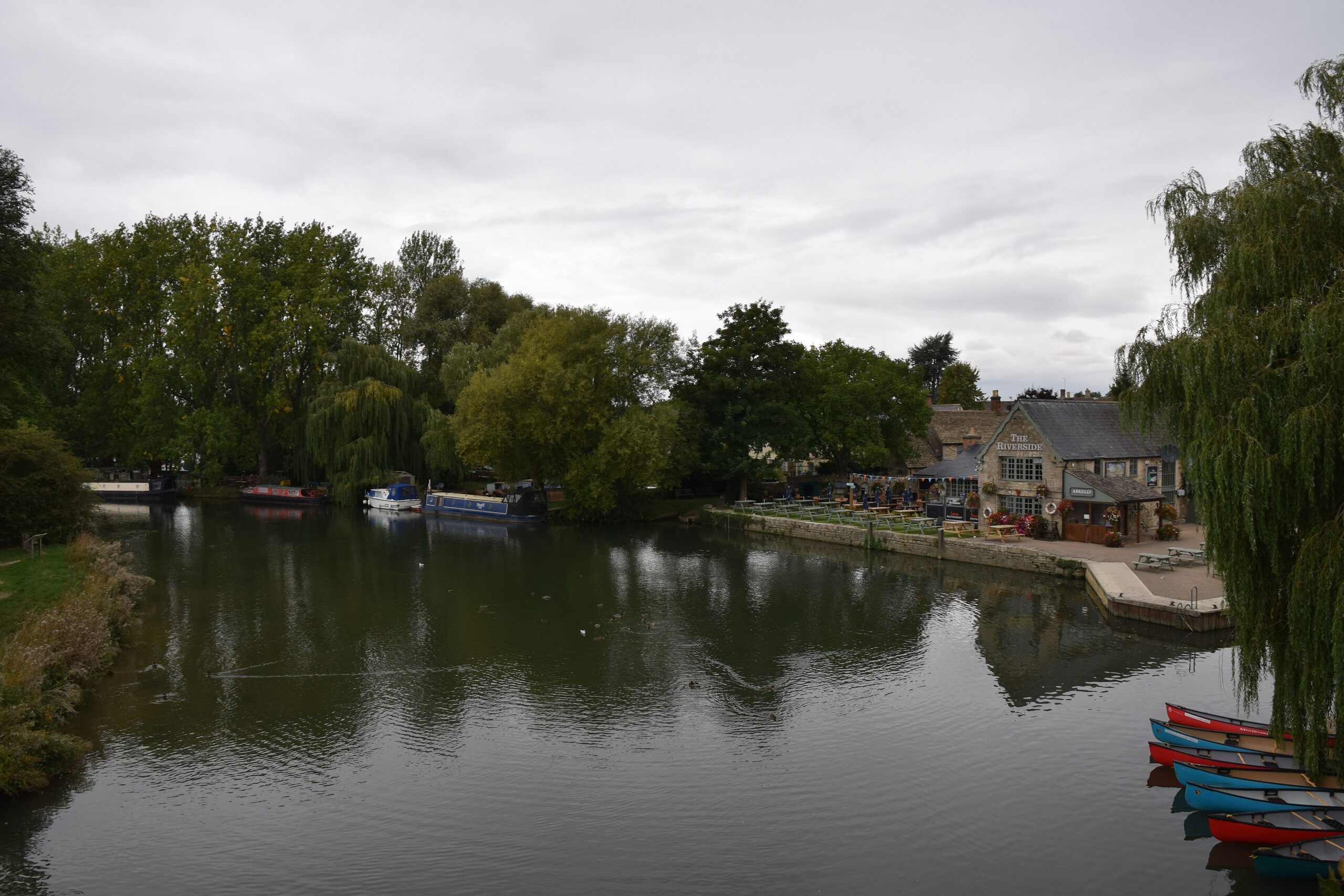 The River Thames at Lechlade with moored boats, rowing boats and riverside willows under a grey sky
