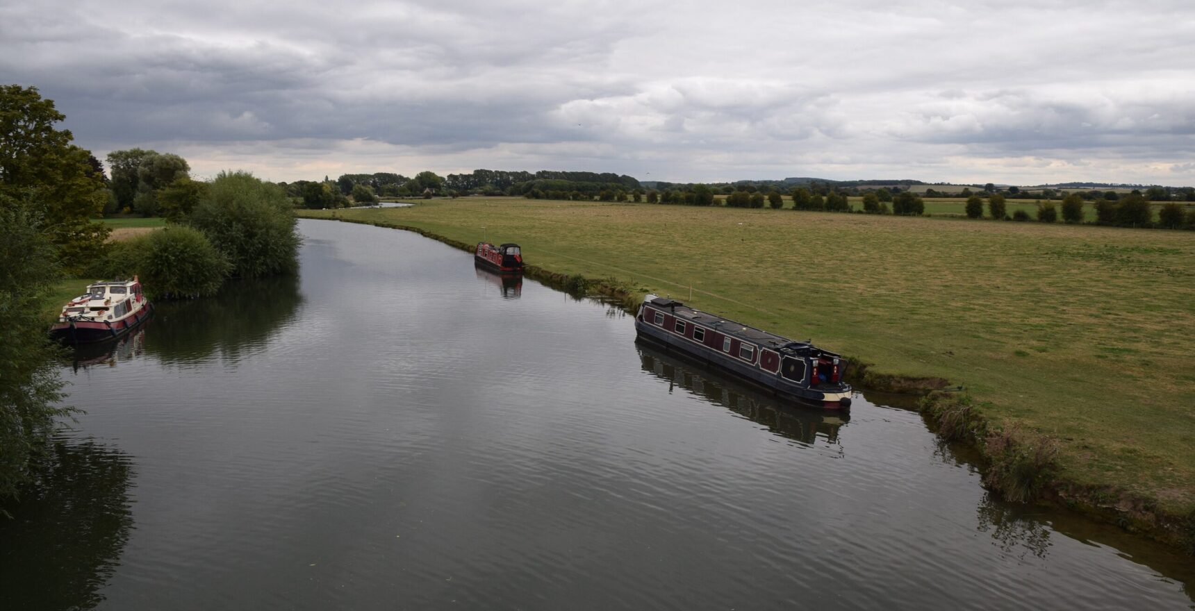 The River Thames winding between flat water meadows below Lechlade, with narrowboats moored along the bank